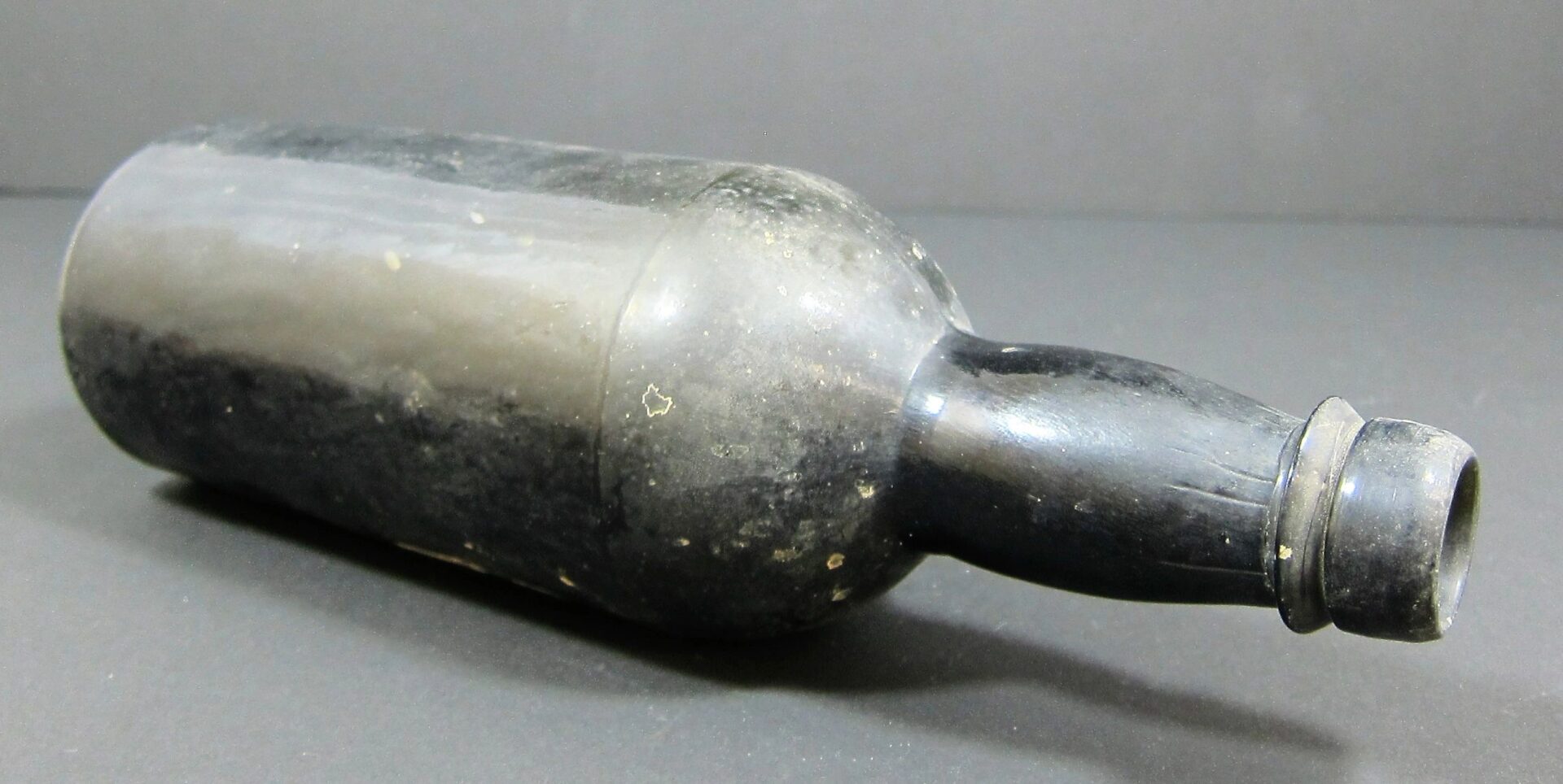 A 19th Century Beer Bottle - Non Excavated with a black glass body, short neck, and slightly bulging form, is shown lying on its side against a plain background.