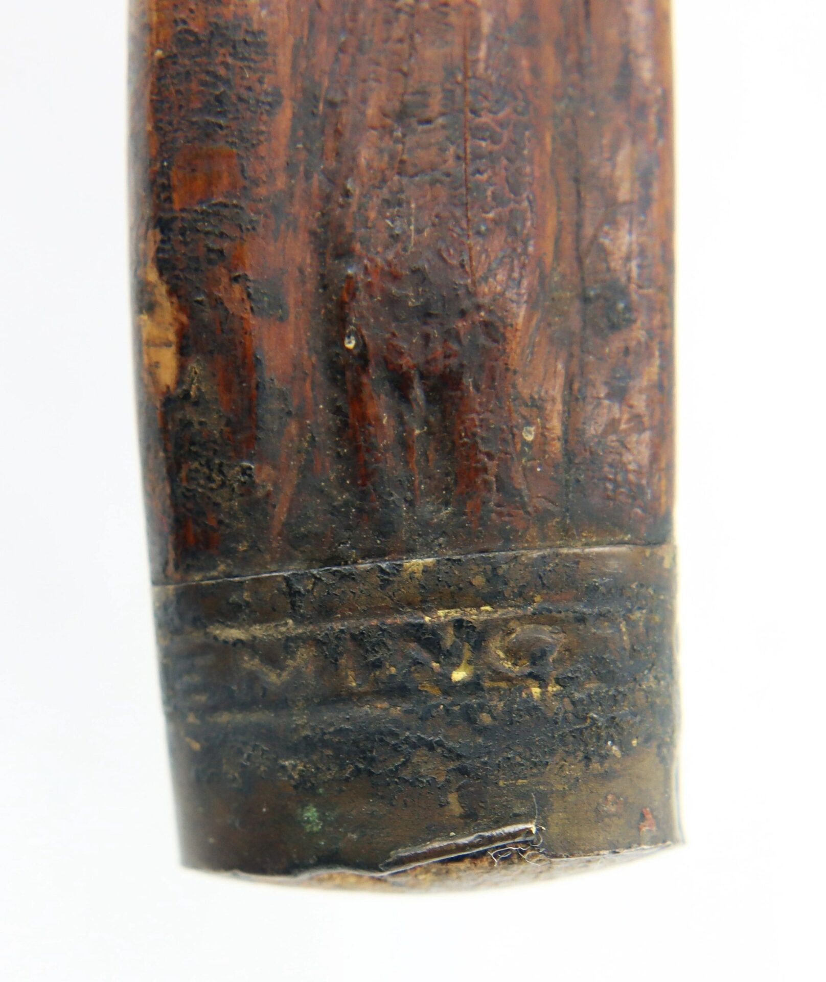 Close-up of a Cane Made of Wood from Georgia Swamp, featuring a worn texture, metal band near the end, and partially visible engraved or stamped letters.