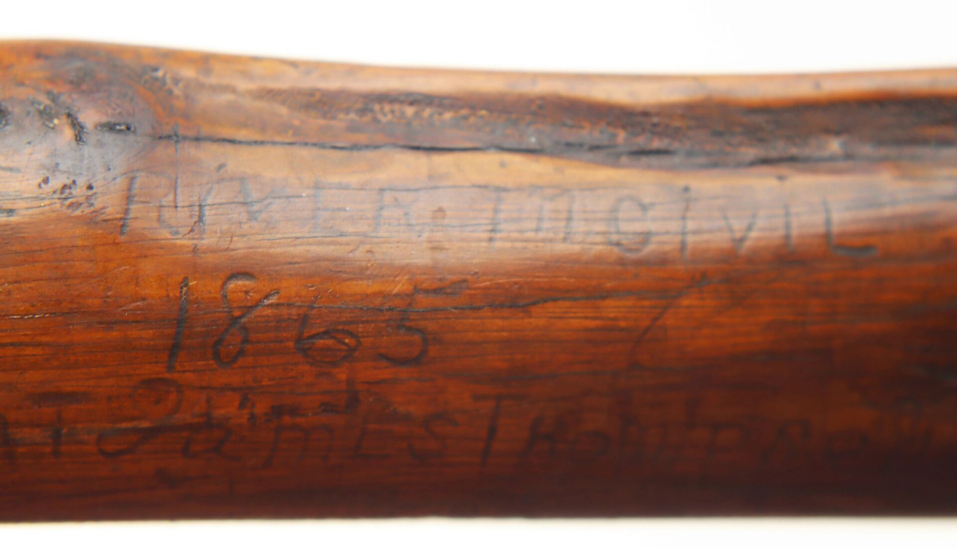 Close-up of the Cane Made of Wood from Georgia Swamp, showing a wooden surface with faintly carved text "CIVIL 1865" and other less legible markings.