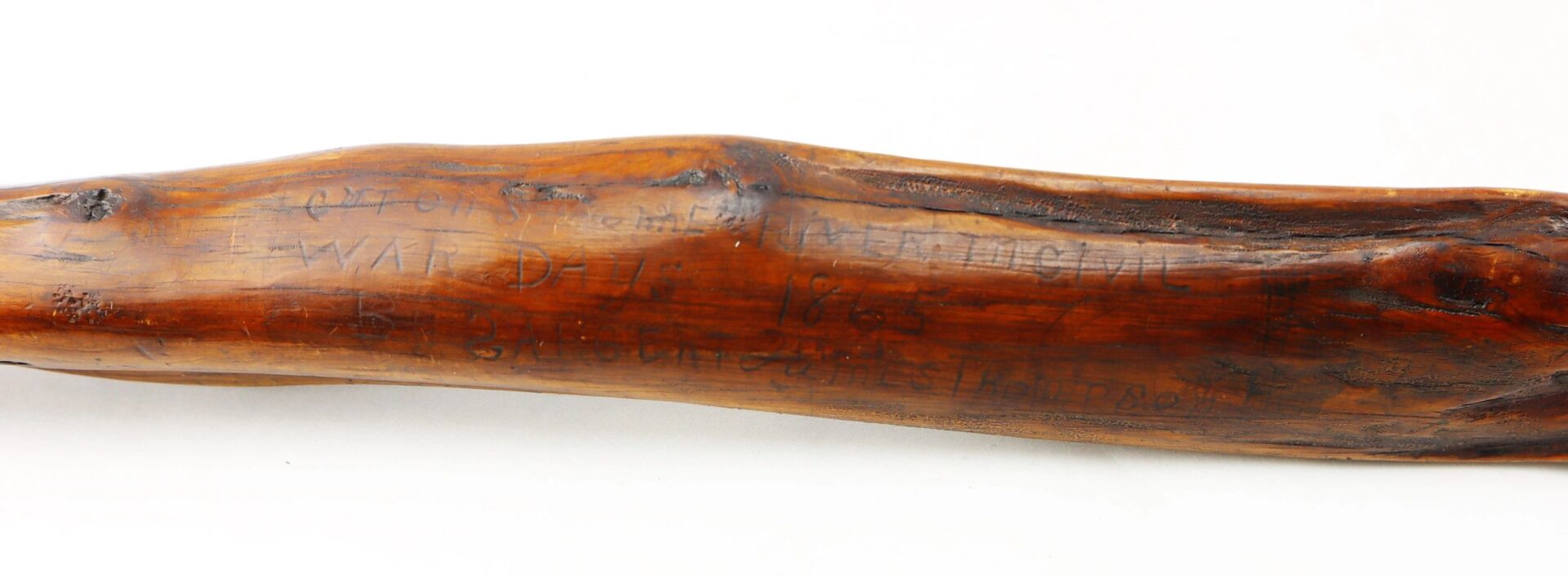 A close-up of the Cane Made of Wood from Georgia Swamp, showing polished wood with faint, hand-carved inscriptions, including the year 1885.