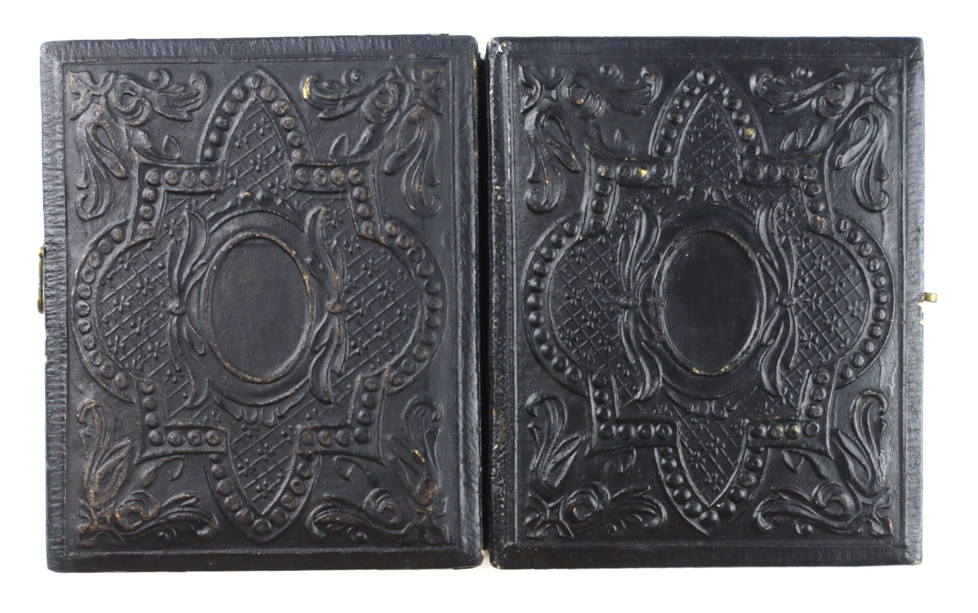 An open, empty antique daguerreotype case with ornate, embossed black covers featuring symmetrical floral and geometric patterns—originally held the "Confederate Soldier with Piccolo!" photograph.