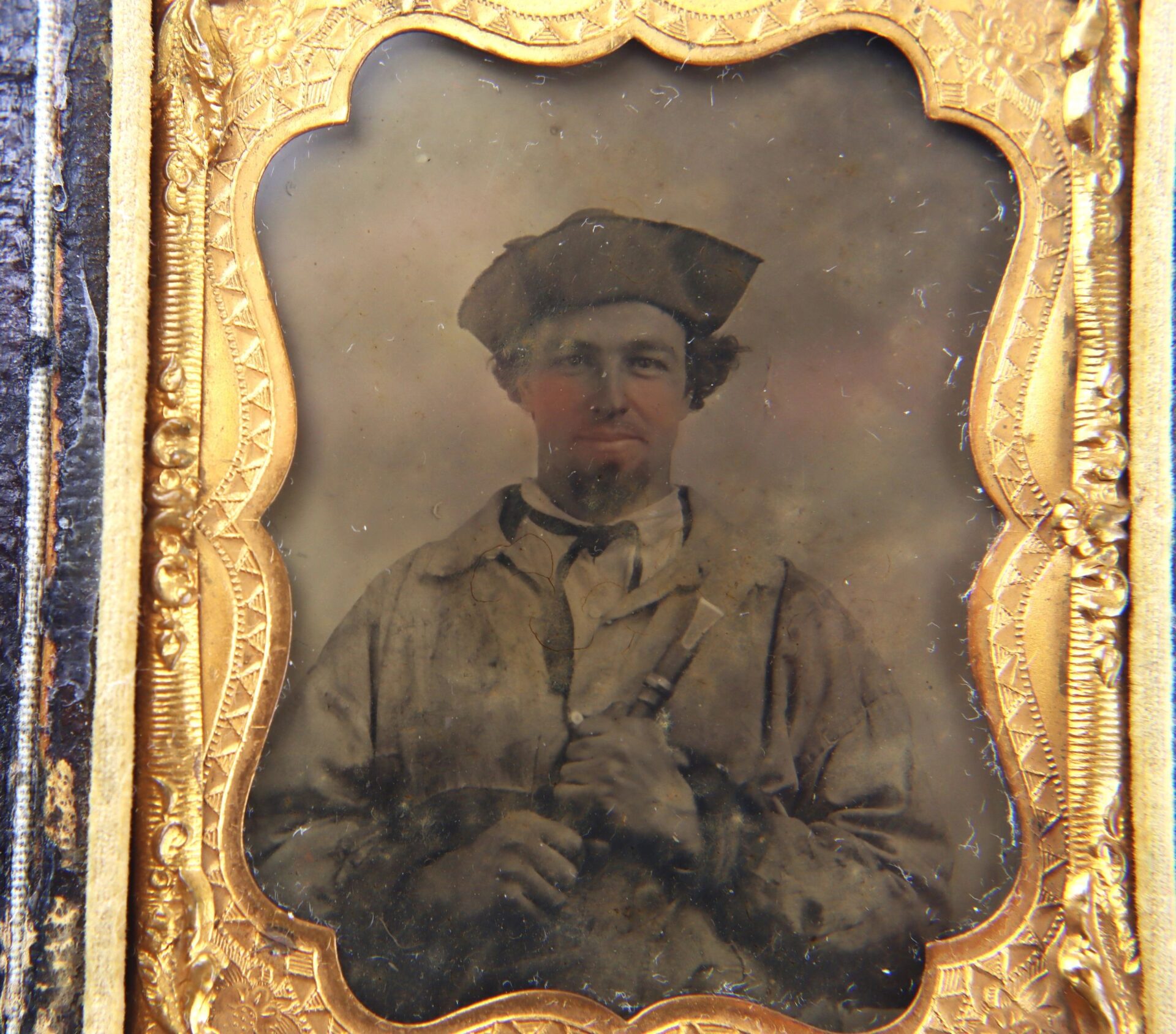 A sepia photo of a Confederate soldier wearing a hat and holding a piccolo, framed in an ornate gold case.