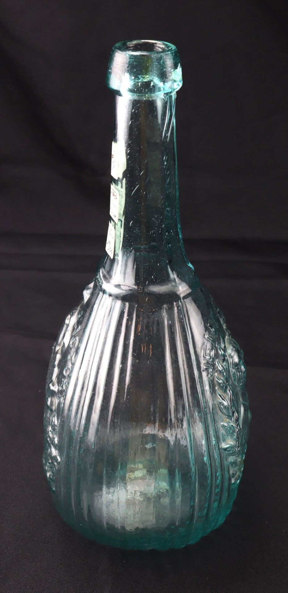 An Aqua "Jenny Lind" Flask with a vintage blue-green hue, featuring vertical ribbing and embossed details, displayed against a black background.