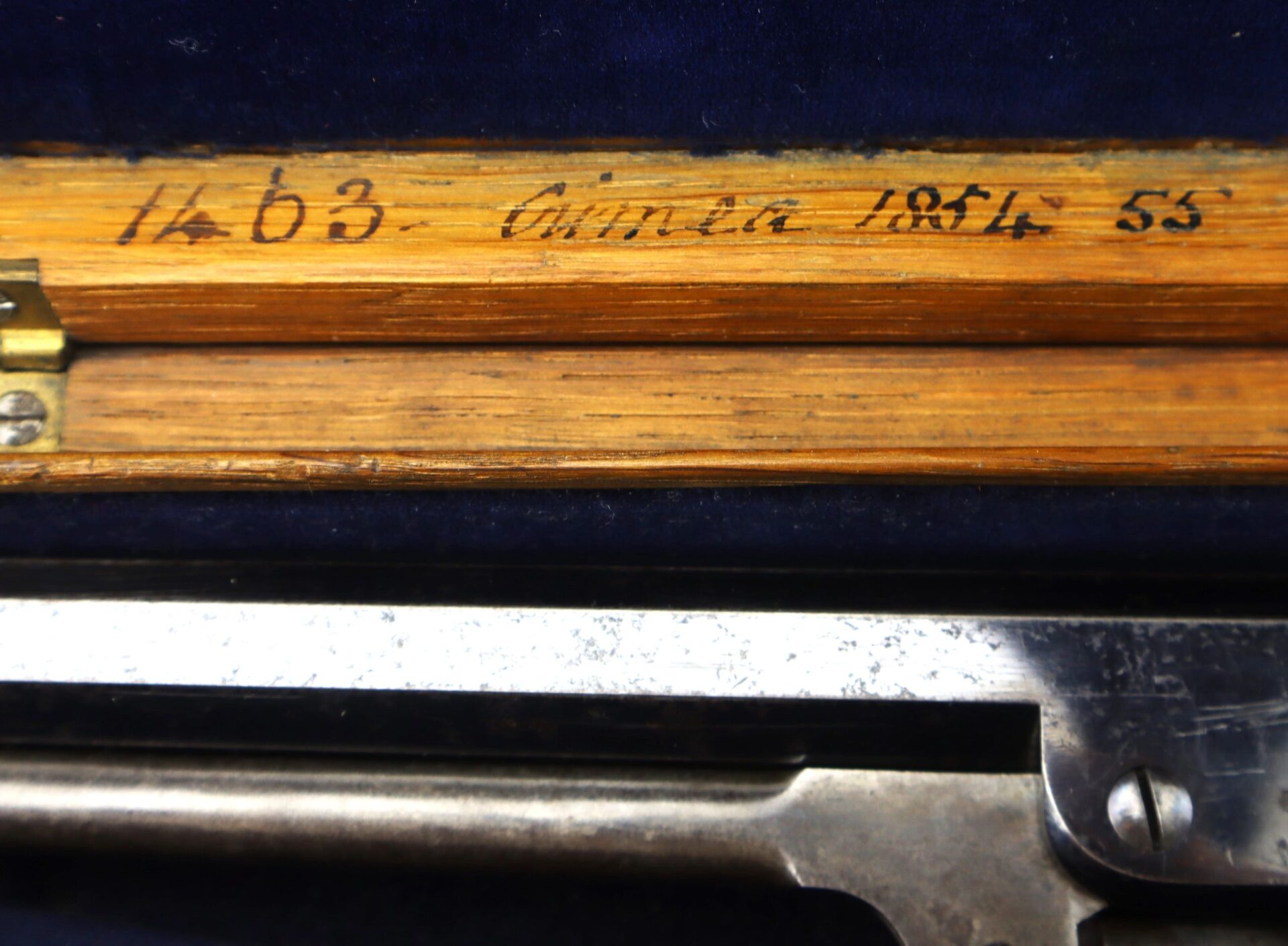 Close-up of a wooden case for a Cased High Condition London Colt 1851 Navy Percussion Revolver, featuring handwritten numbers and text, with part of the metallic revolver visible inside.