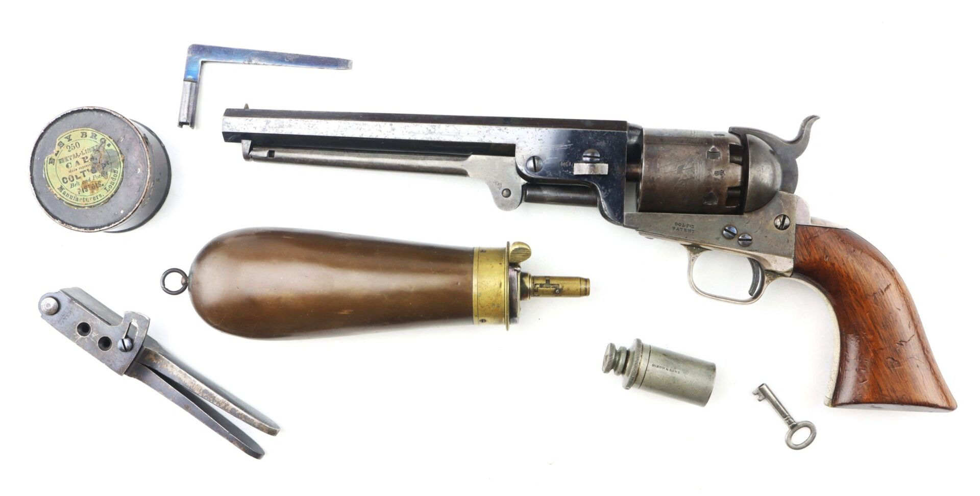 A Cased High Condition London Colt 1851 Navy Percussion Revolver with wooden grip, powder flask, bullet mold, percussion caps tin, key, wrench, and a small container displayed on a white background.