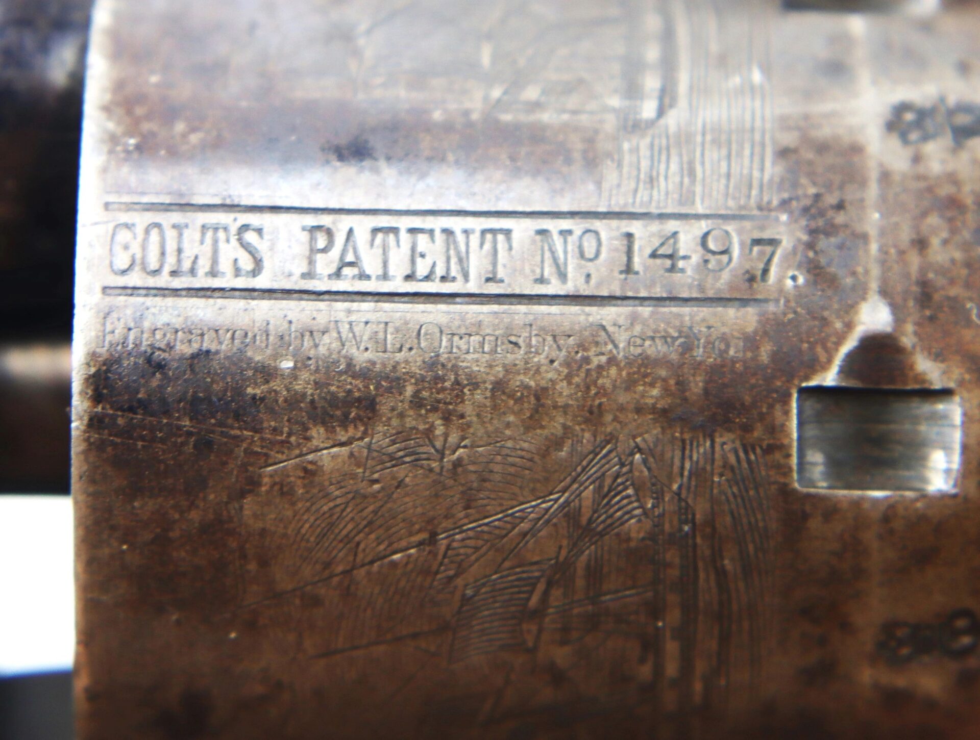 Close-up of the metal surface on a Cased High Condition London Colt 1851 Navy Percussion Revolver, engraved with "COLT'S PATENT No 1497" and faint additional text, showing wear and aging.
