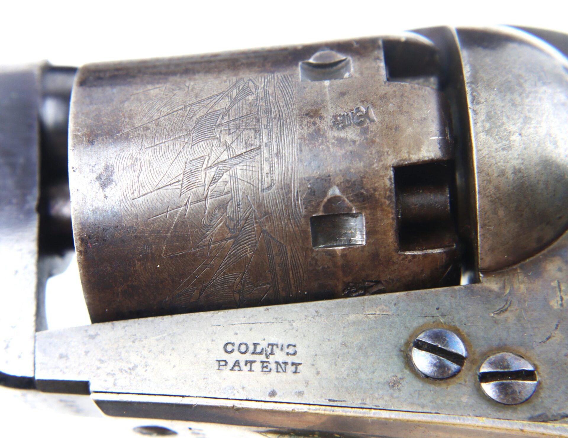 Close-up view of the Cased High Condition London Colt 1851 Navy Percussion Revolverās weathered cylinder, displaying engraved markings and "COLT'S PATENT" on the metal plate below.