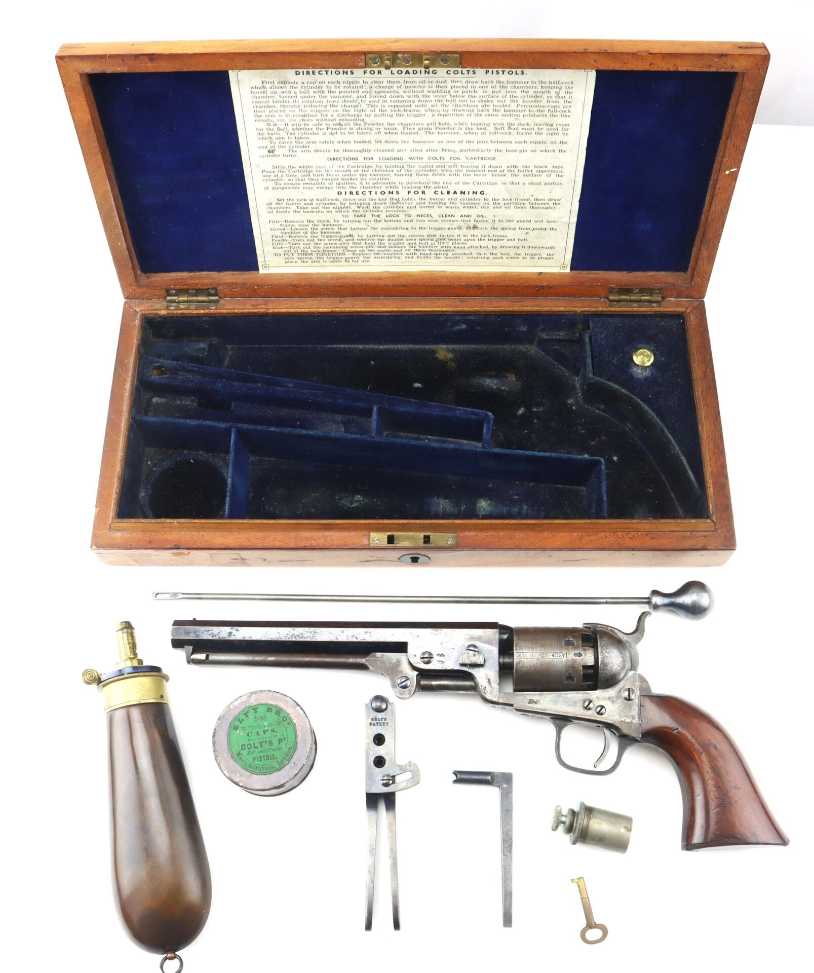 Cased London Colt 1851 Navy Percussion Revolver with accessories, displayed in an open wooden box lined with blue velvet, containing the revolver, powder flask, bullets, tools, and neatly arranged contents.