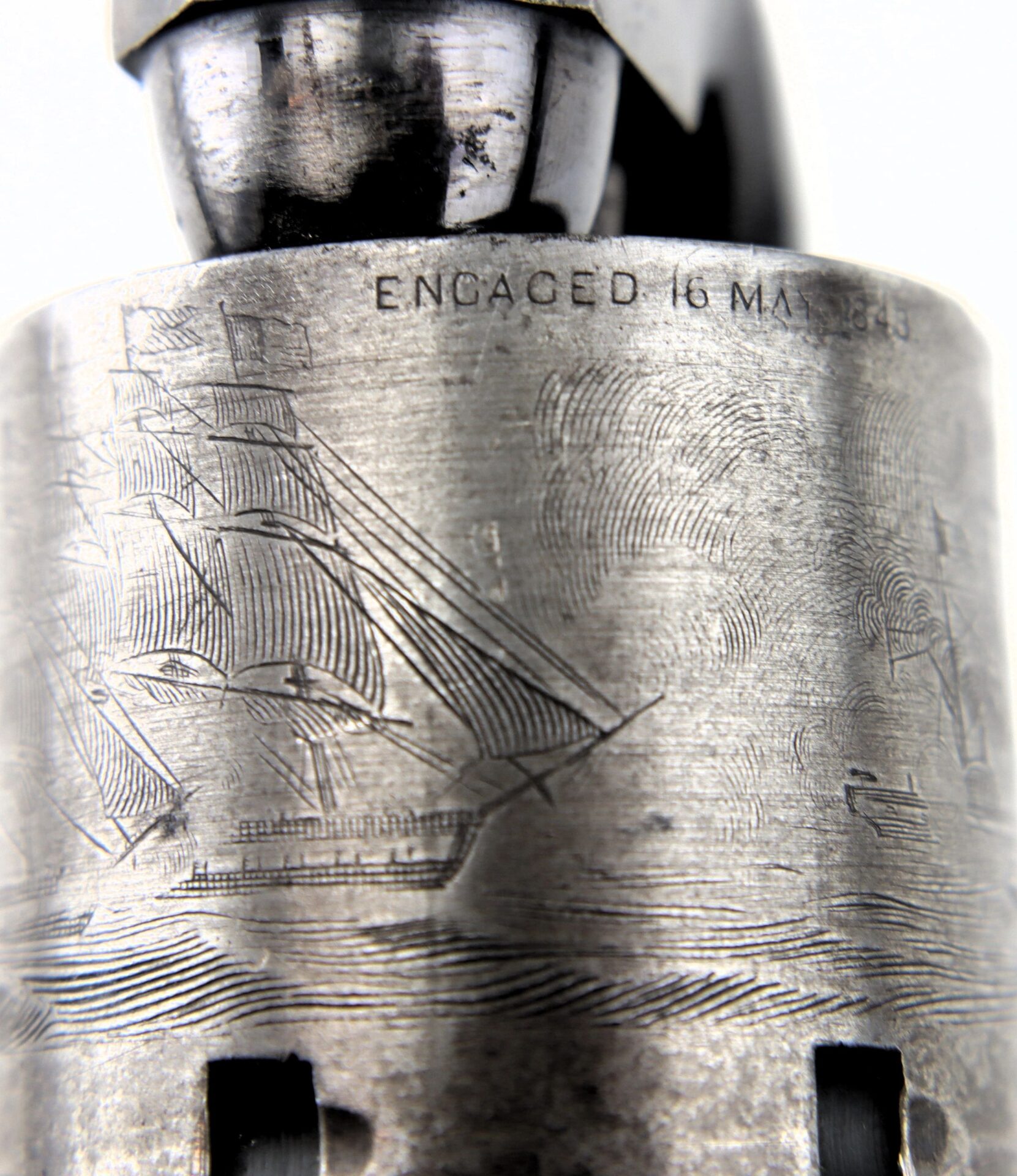 Close-up of an engraved metal surface on a Cased London Colt 1851 Navy Percussion Revolver, featuring a sailing ship and the inscription "ENGAGED 16 MAY 1843" above the image.