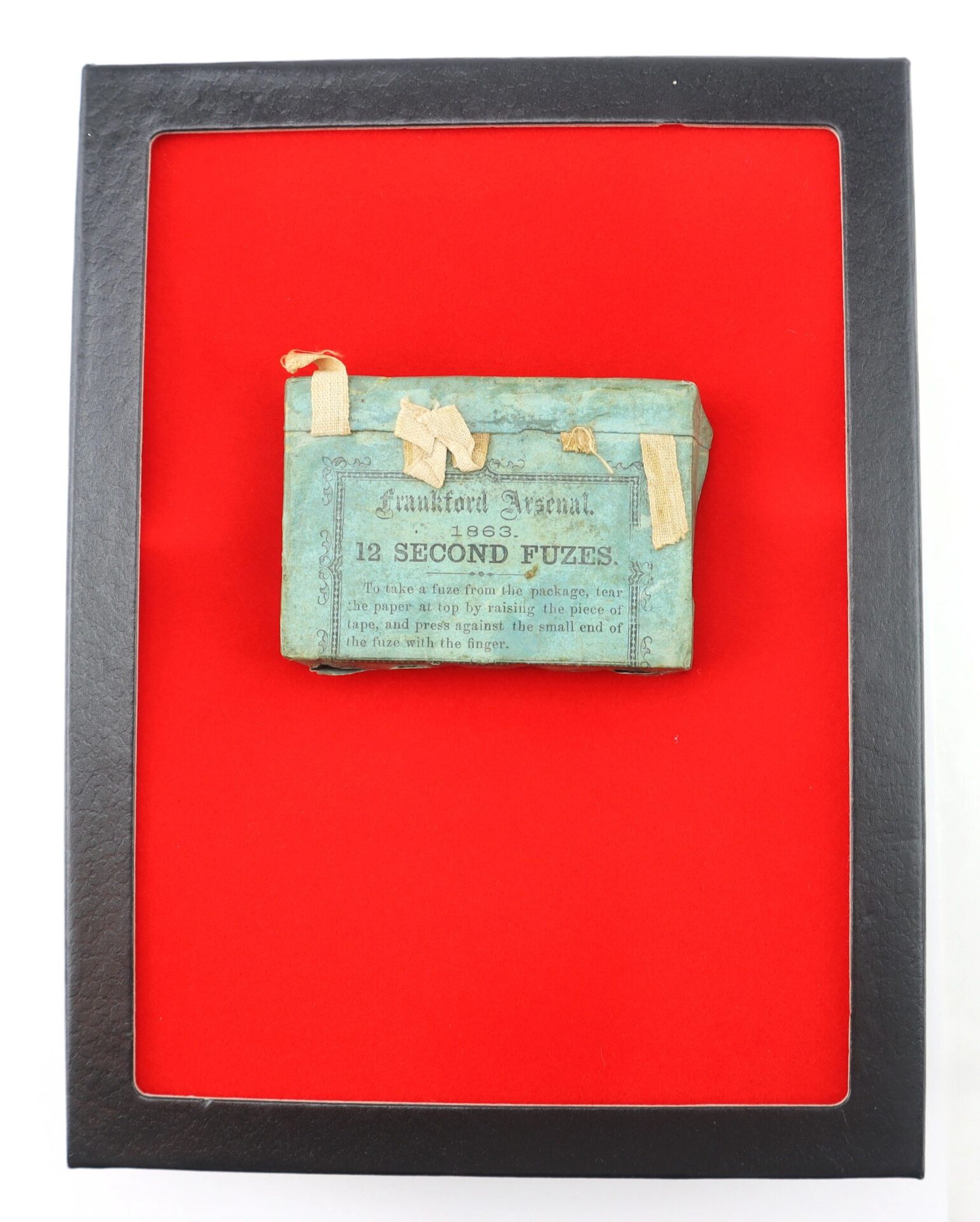 A Frankford Arsenal 12 Second Fuses box (blue, 1883) is displayed in a black frame set against a vivid red background.