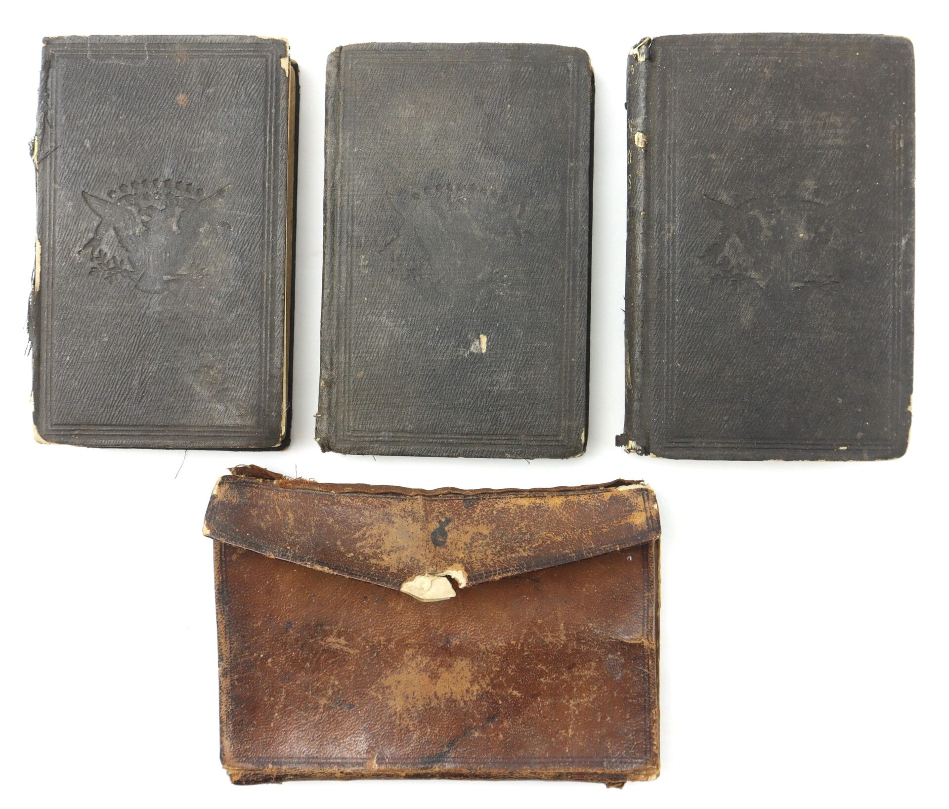 Three worn, dark-covered books from the 10th Tennessee Volunteer Infantry (Union) Grouping are displayed above a brown, weathered leather pouch with a flap and broken clasp on a white background.