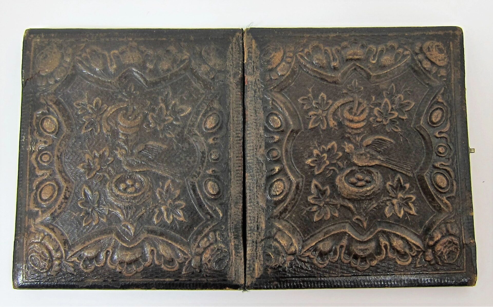 A Union Engineer Sixth Plate Tintype in an antique, ornately embossed leather case with floral and bird motifs, shown closed and slightly worn along the spine.