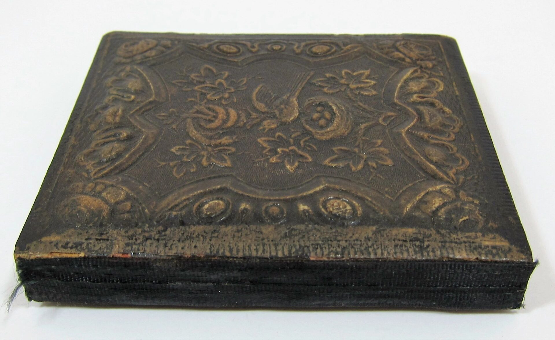 A closed, square vintage Union Engineer Sixth Plate Tintype case with an embossed floral and shell pattern on its worn, dark cover.