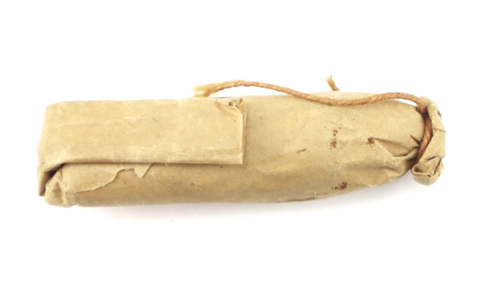 A .58 caliber 1855 Rifle Musket Cartridge, rectangular and small, wrapped in brown paper with a string tied at one end, is shown on a white background.