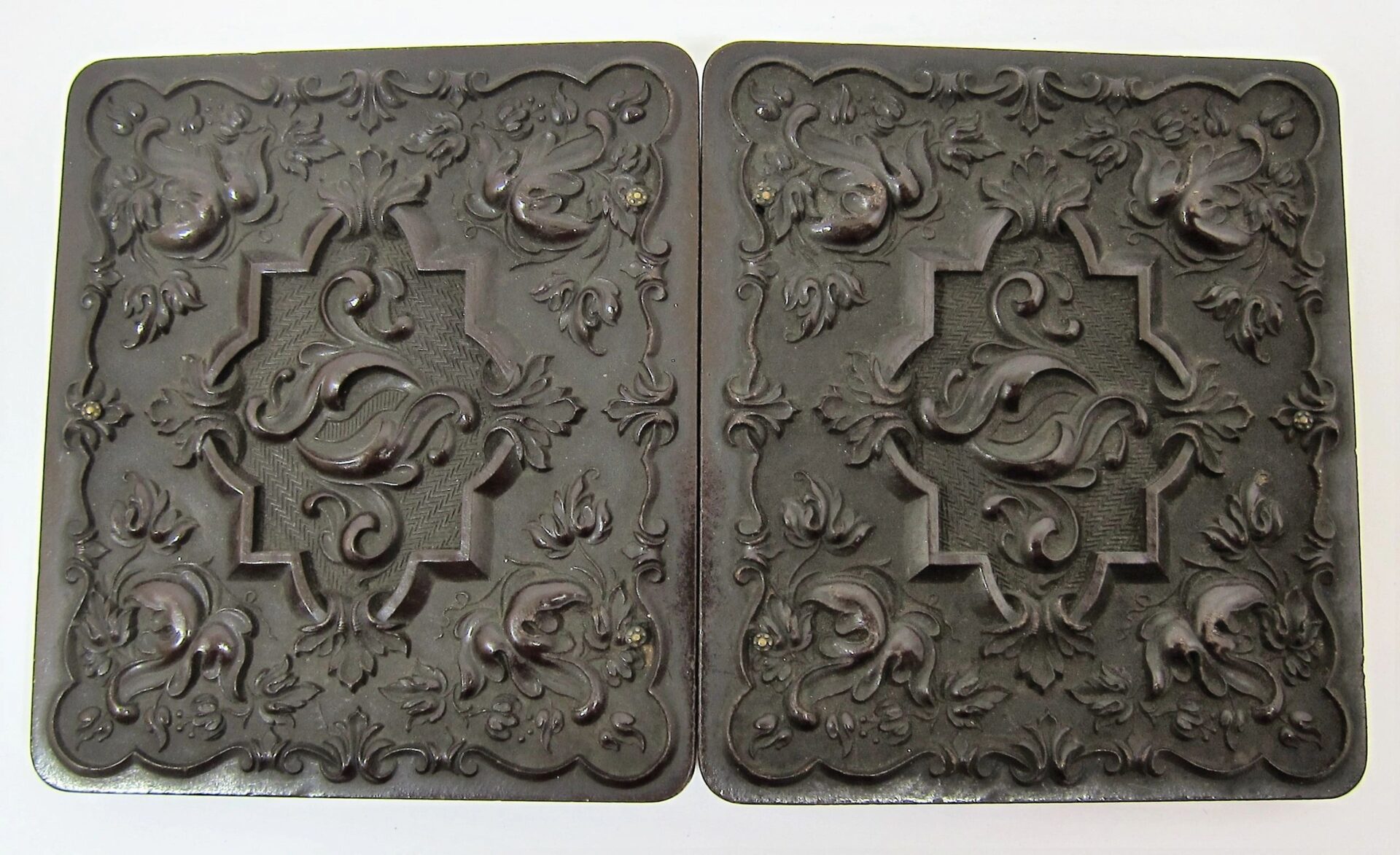 A pair of ornate, square, dark cases with raised floral and scroll patterns and a central shield on each lid for an Infantry Officer Holding Musket Sixth Plate Tintype.
