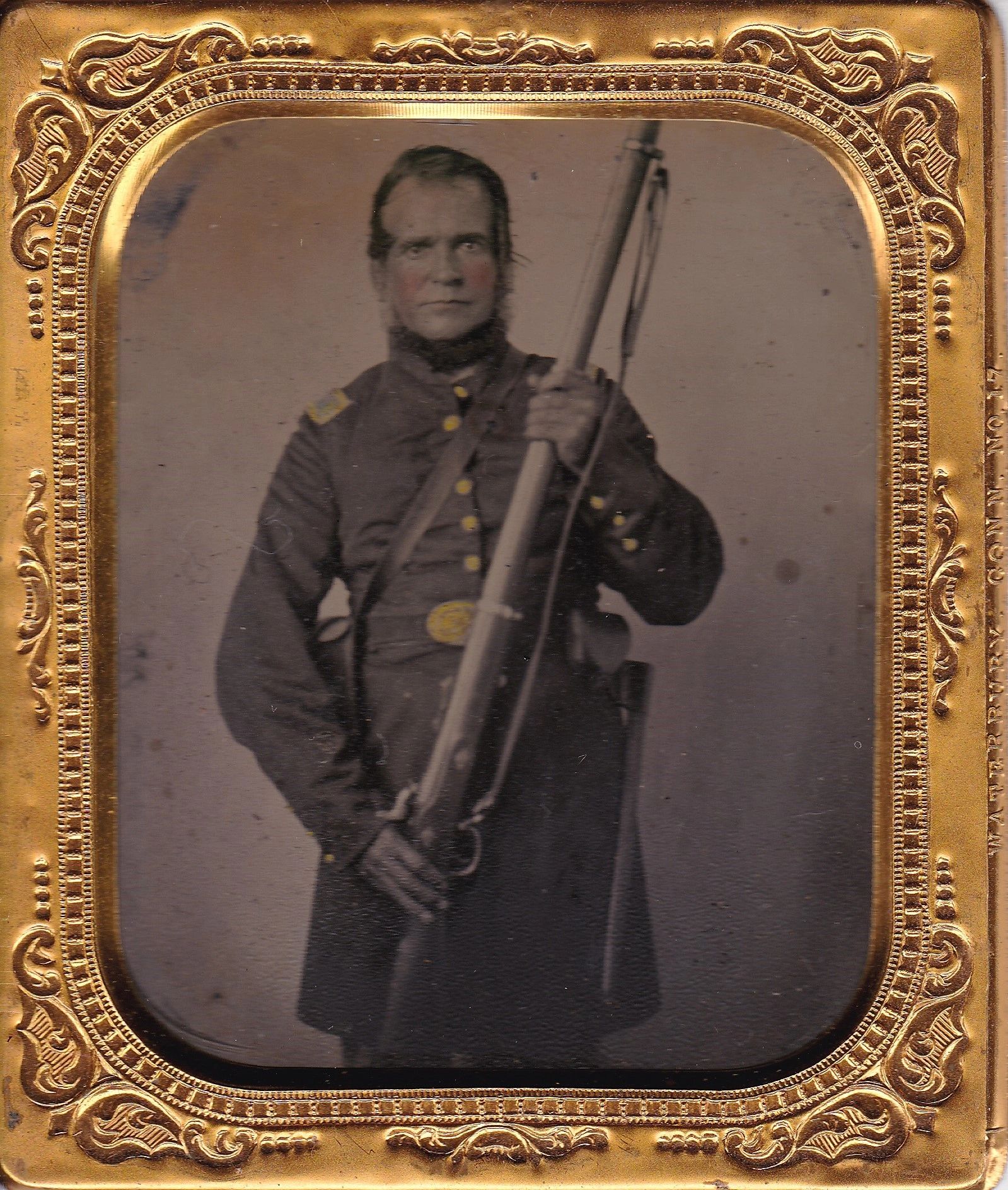 An Infantry Officer in a 19th-century uniform holds a musket, captured in a Sixth Plate Tintype and displayed in an ornate gold case.