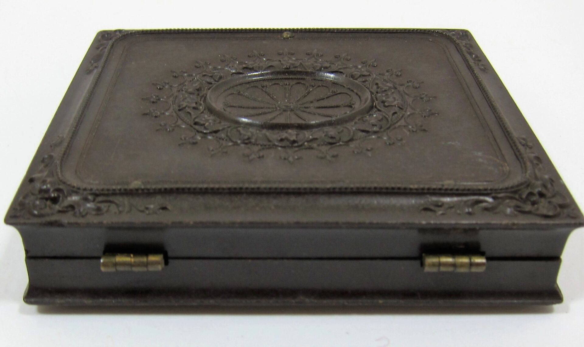 A closed, rectangular, dark brown vintage case with ornate floral patterns and two small brass hinges on the front, containing a 2nd Infantry Regiment Company "I" Sixth Plate Tintype.