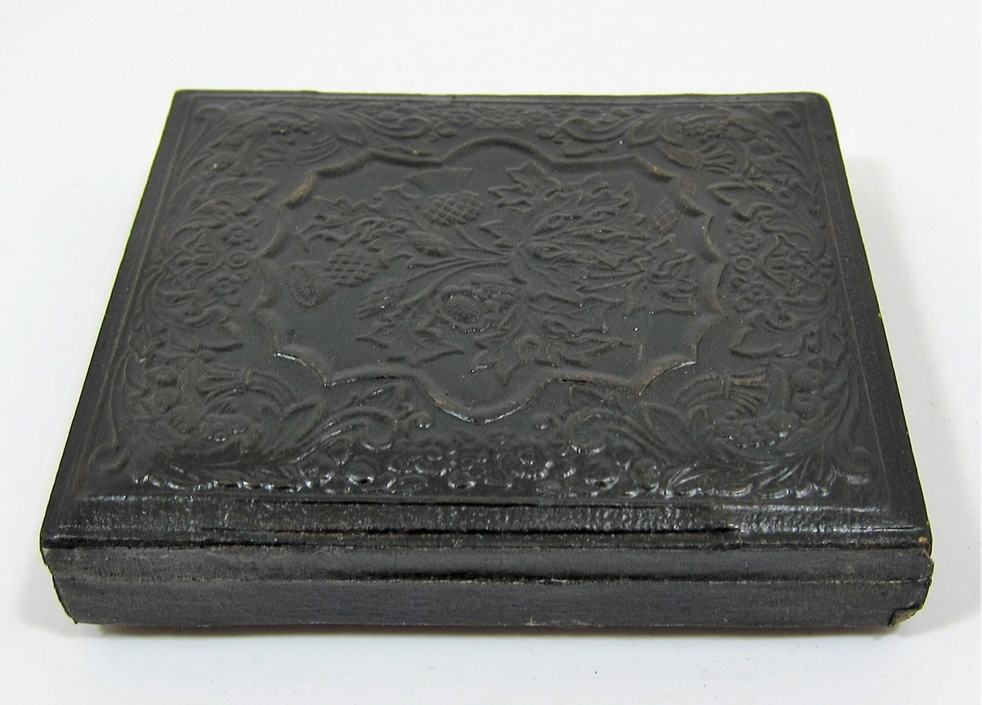A closed, square, black case with ornate floral and geometric embossing on the lid holds the "Soldier with Model 1816 Musket Sixth Plate Tintype," displayed against a plain white background.