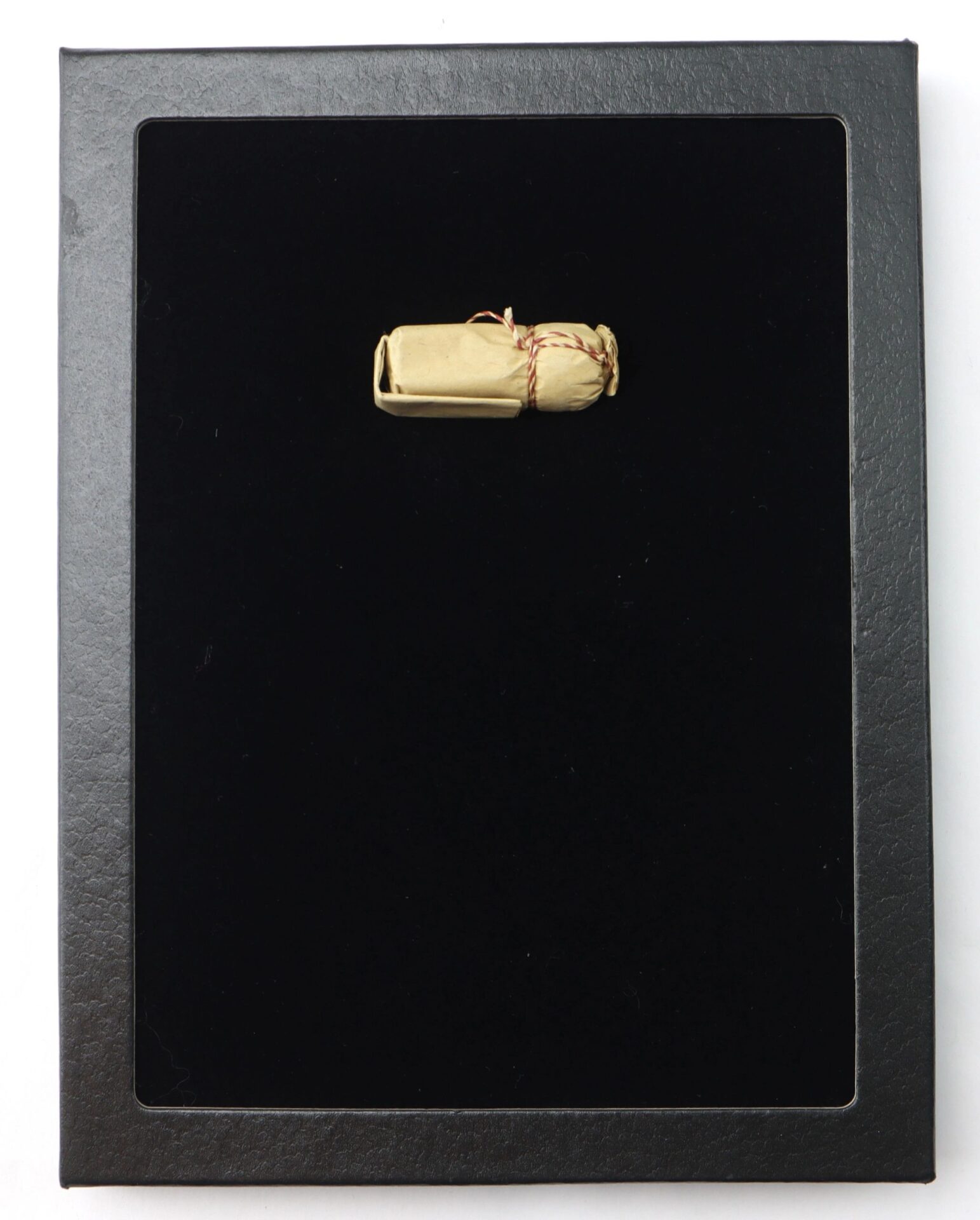 A .69 Caliber Hall Carbine Cartridge, small and rolled with twine, is centered on a black matte background inside a black frame.