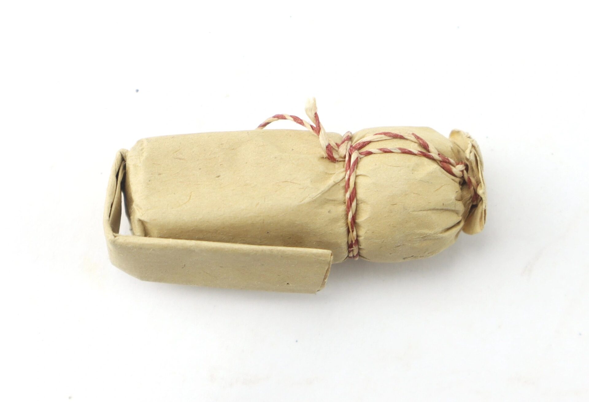 A .69 Caliber Hall Carbine Cartridge wrapped in brown paper and tied with red and white string, displayed on a white background.