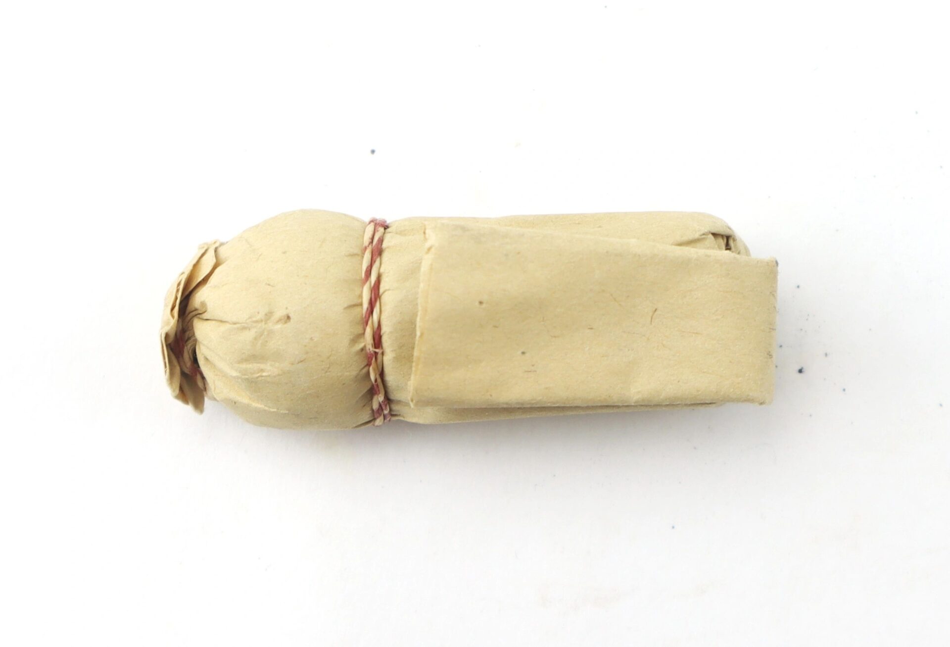 A .69 Caliber Hall Carbine Cartridge, wrapped in brown paper and tied with red and white string, is displayed on a white background.