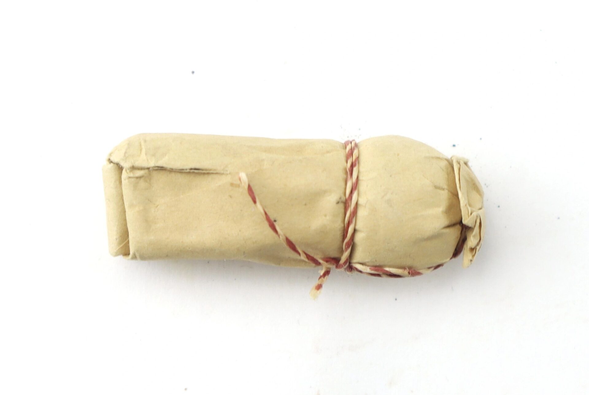 A .69 Caliber Hall Carbine Cartridge is shown wrapped in brown paper and tied with red and white string, photographed against a white background.