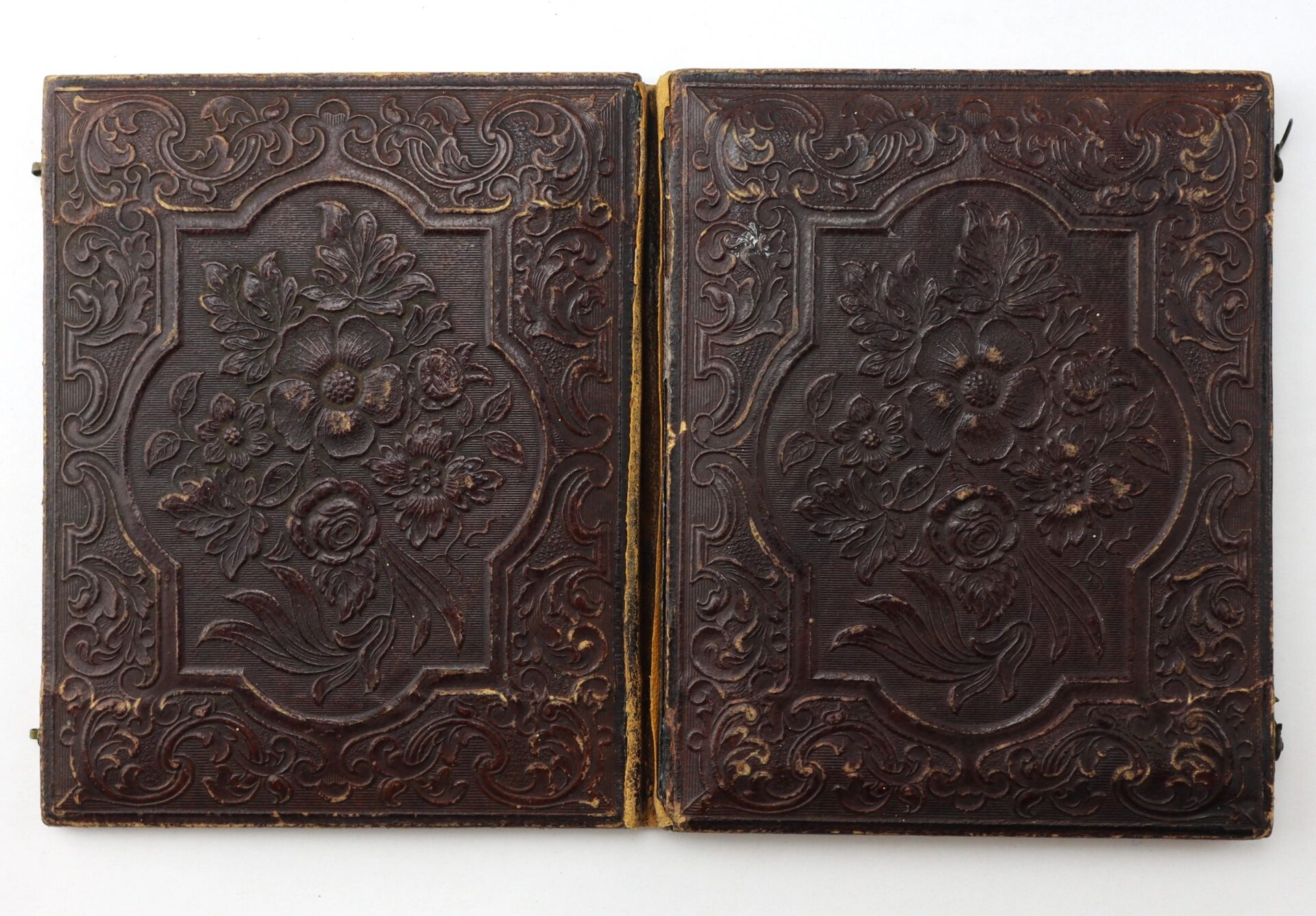 A 1/4 Plate Tintype of two Union musicians in Hardee hats, housed in dark brown antique embossed leather photo case covers with floral designs and decorative borders, shown closed against a white background.
