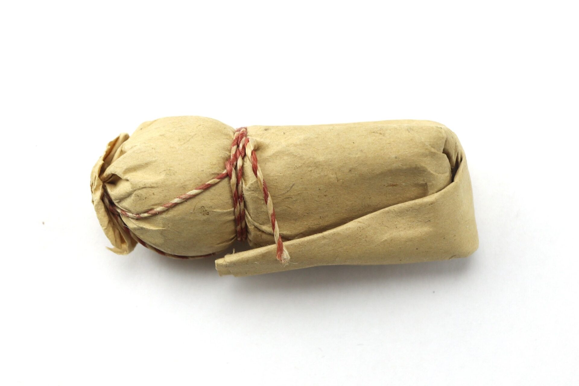 A .69 Caliber Hall Carbine Cartridge, rolled in brown paper and tied with red and white string, rests on a white background.