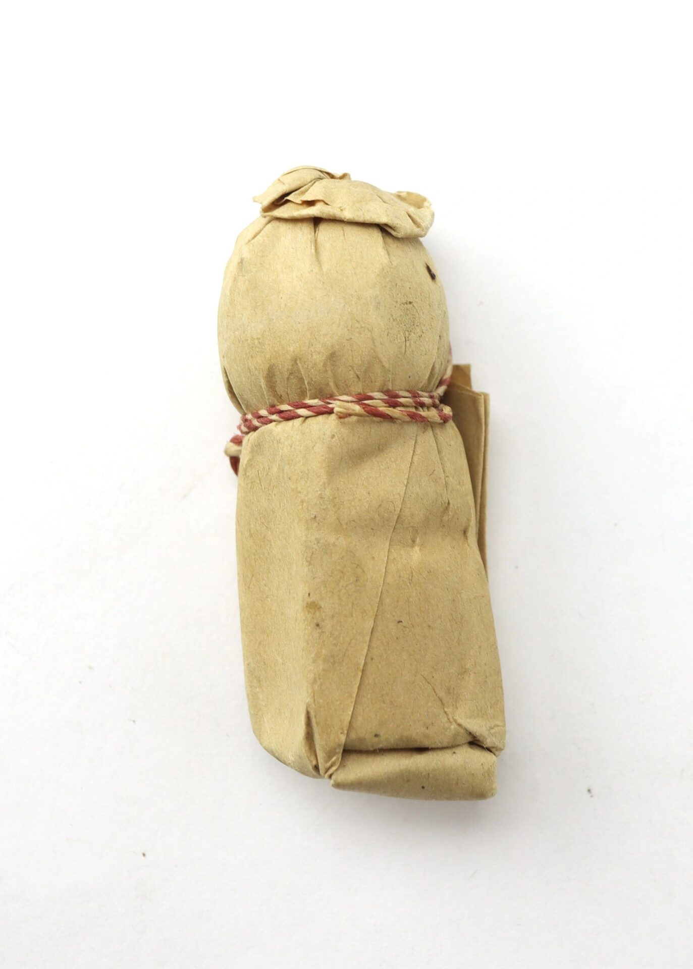 A .69 Caliber Hall Carbine Cartridge, wrapped in brown paper and tied with red and white string, stands upright against a plain white background.