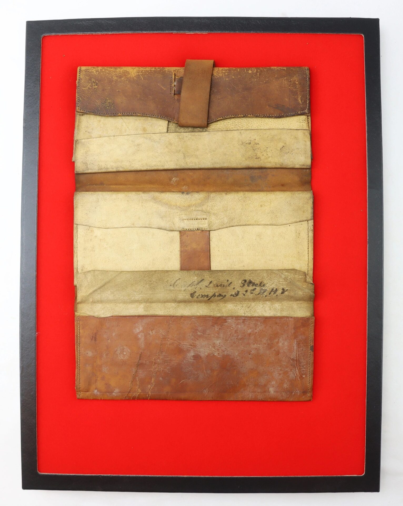 The Inscribed Wallet of Corporal David Steele, 2nd New Hampshire Infantry (ON-HOLD), is a worn brown leather and canvas pouch with handwritten text, displayed on a bright red background inside a black frame.