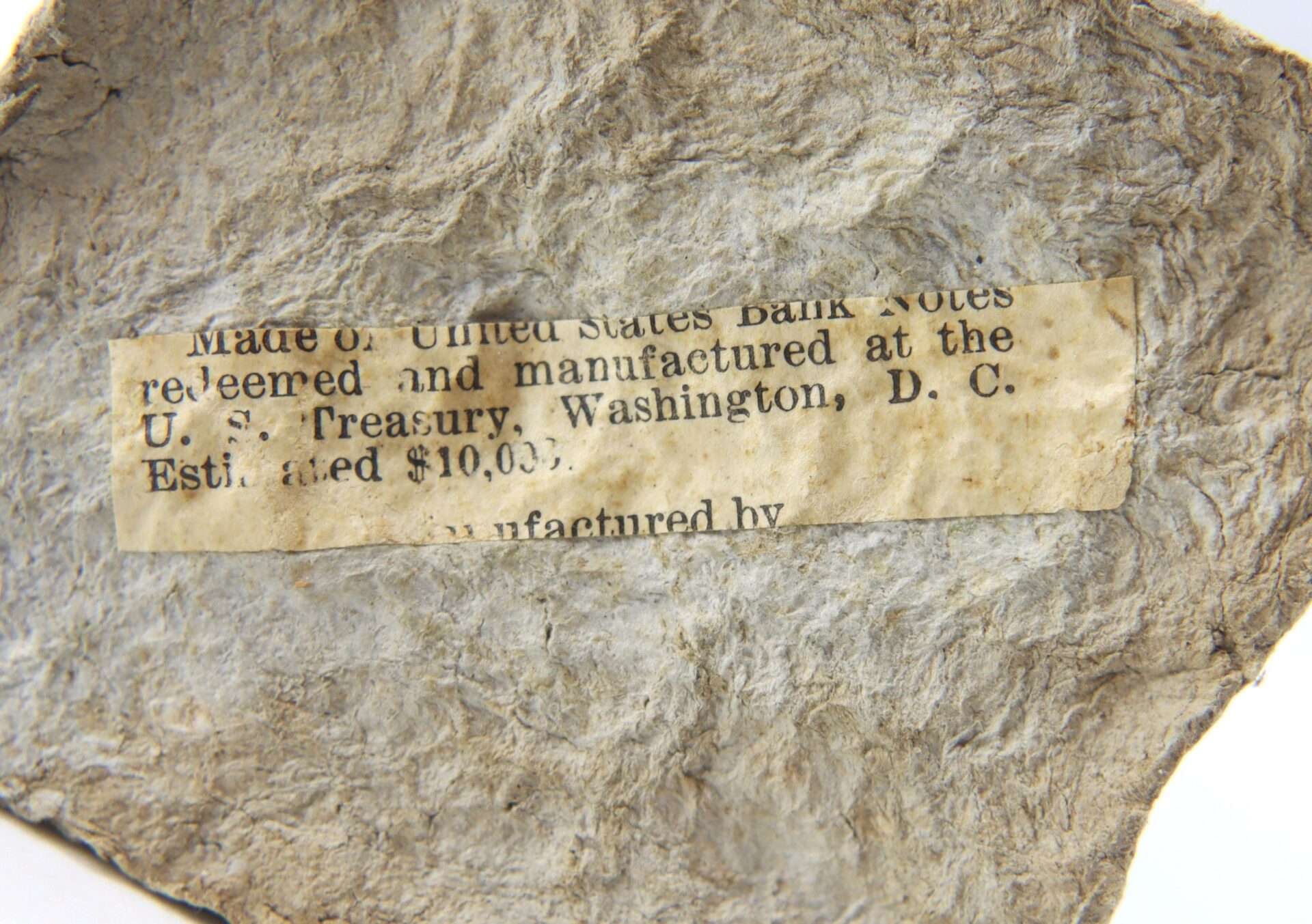 A small, worn label on the Washington Monument Made from macerated U.S. Currency reads: "Made of United States Bank Notes redeemed and manufactured at the U.S. Treasury, Washington, D.C. Estimated $10.00.