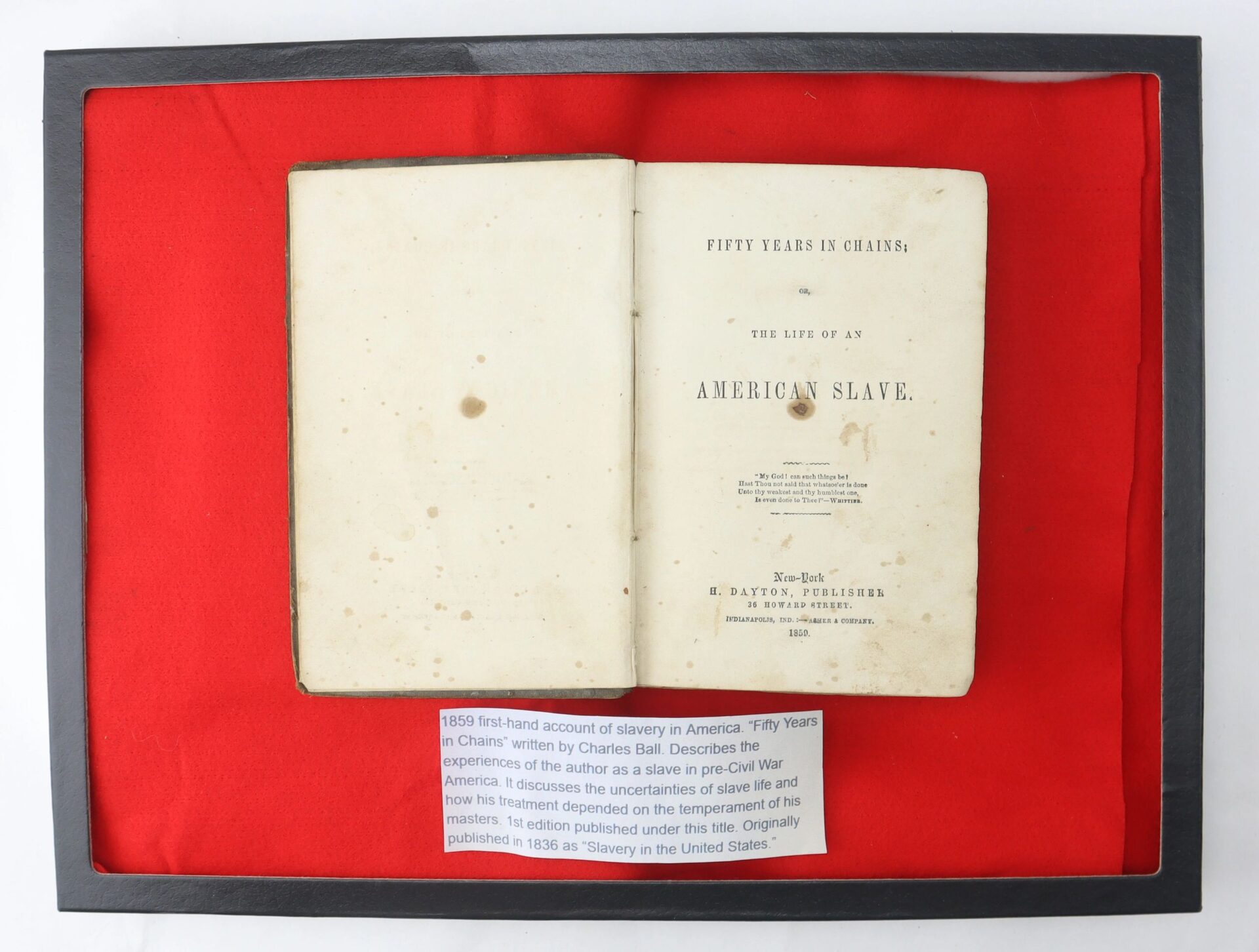 An open book, "Fifty Years in Chains, The Life of an American Slave," rests on red fabric with a plaque beneath it explaining its historical significance.