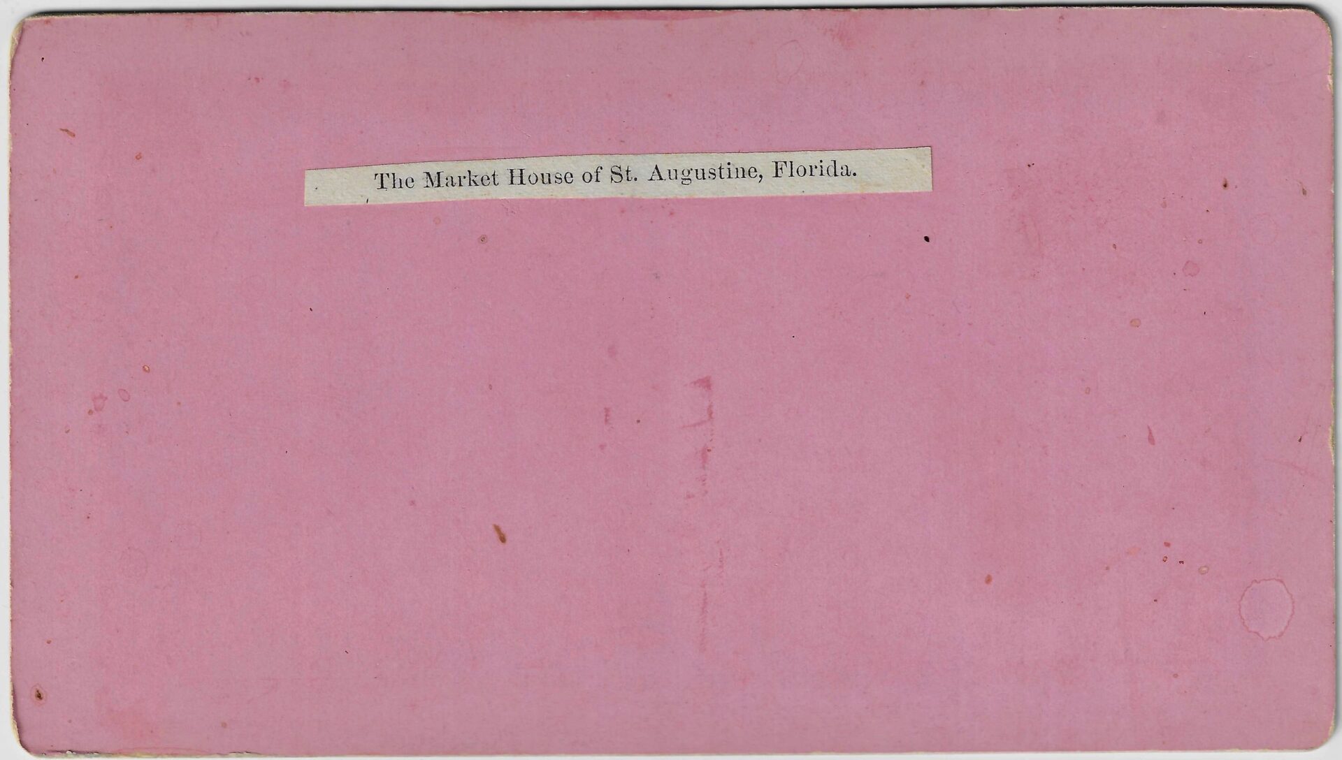 A pink card featuring a white label at the center that reads: The Market House of Saint Augustine Florida “Formerly a Slave Market”.