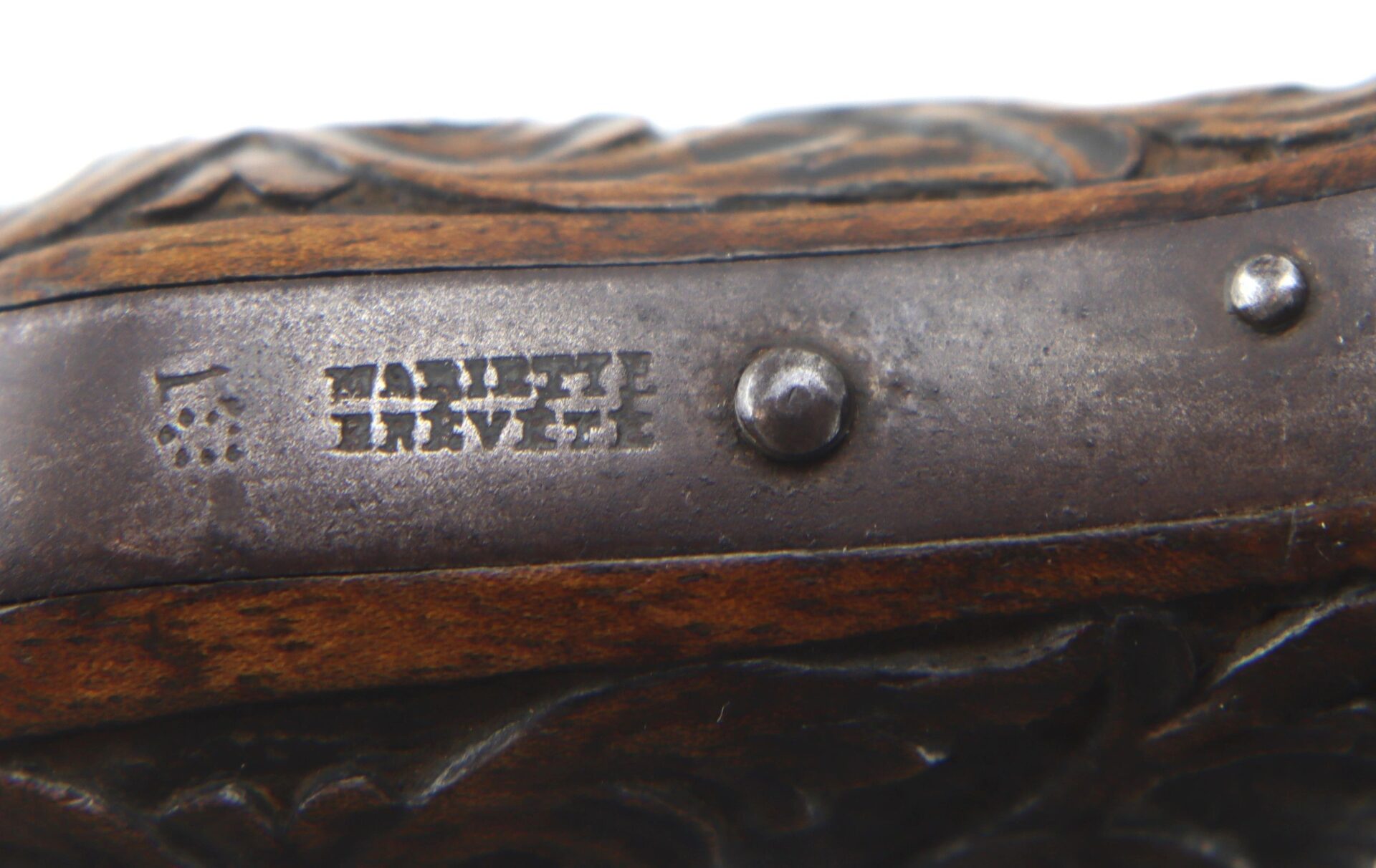 Close-up of a metal plate engraved with “TAUPEE BREVETE” and a symbol, affixed to the carved wooden grip of a Five Barrel Pepperbox Revolver.