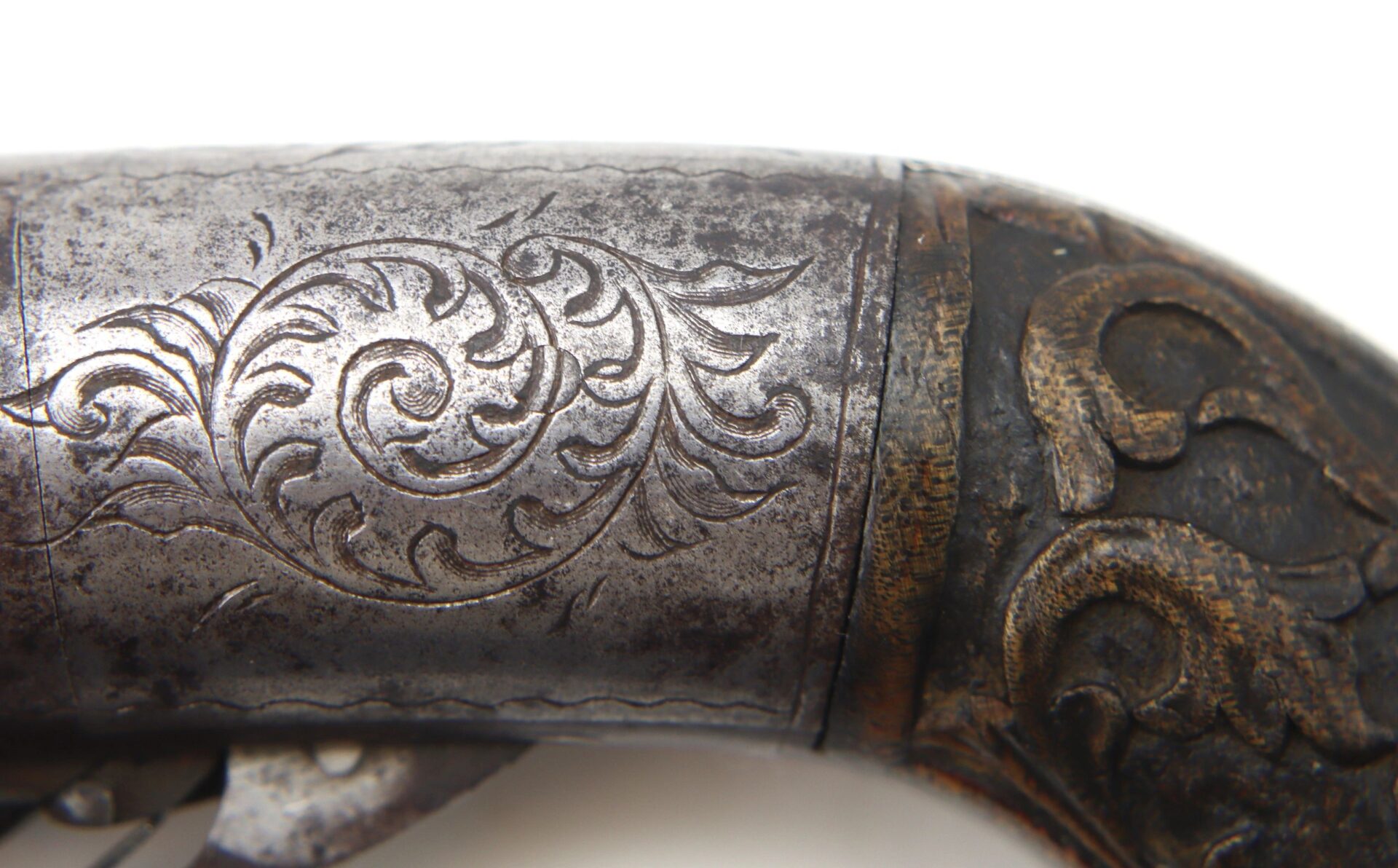 Close-up of a Five Barrel Pepperbox Revolver showing detailed engraved floral patterns on the metal surface and part of the wooden handle.