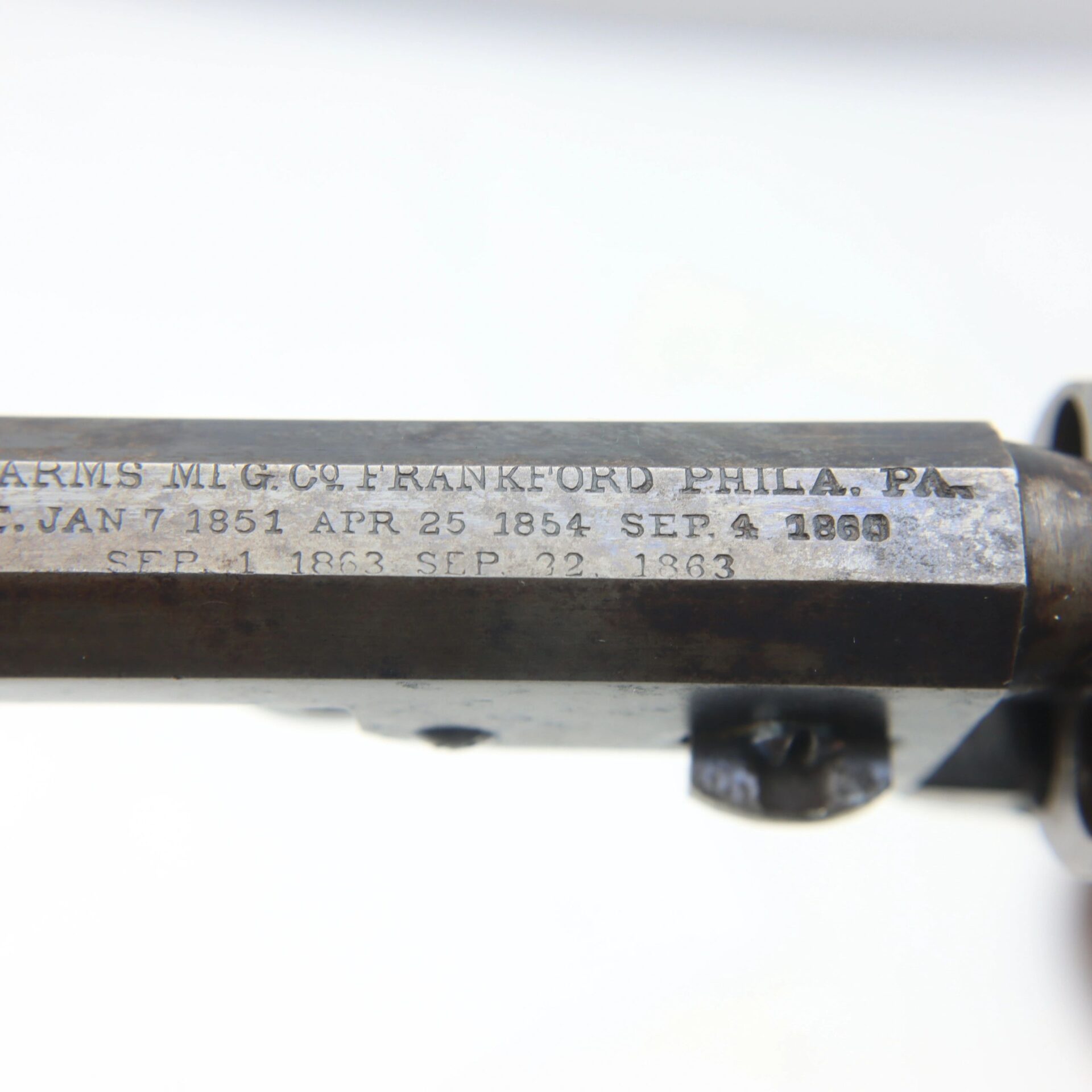 Close-up of engraved text on a Cooper Double Action Revolver's metal barrel, showing date markings and a reference to Frankford, Philadelphia, PA; some dates appear partially worn.