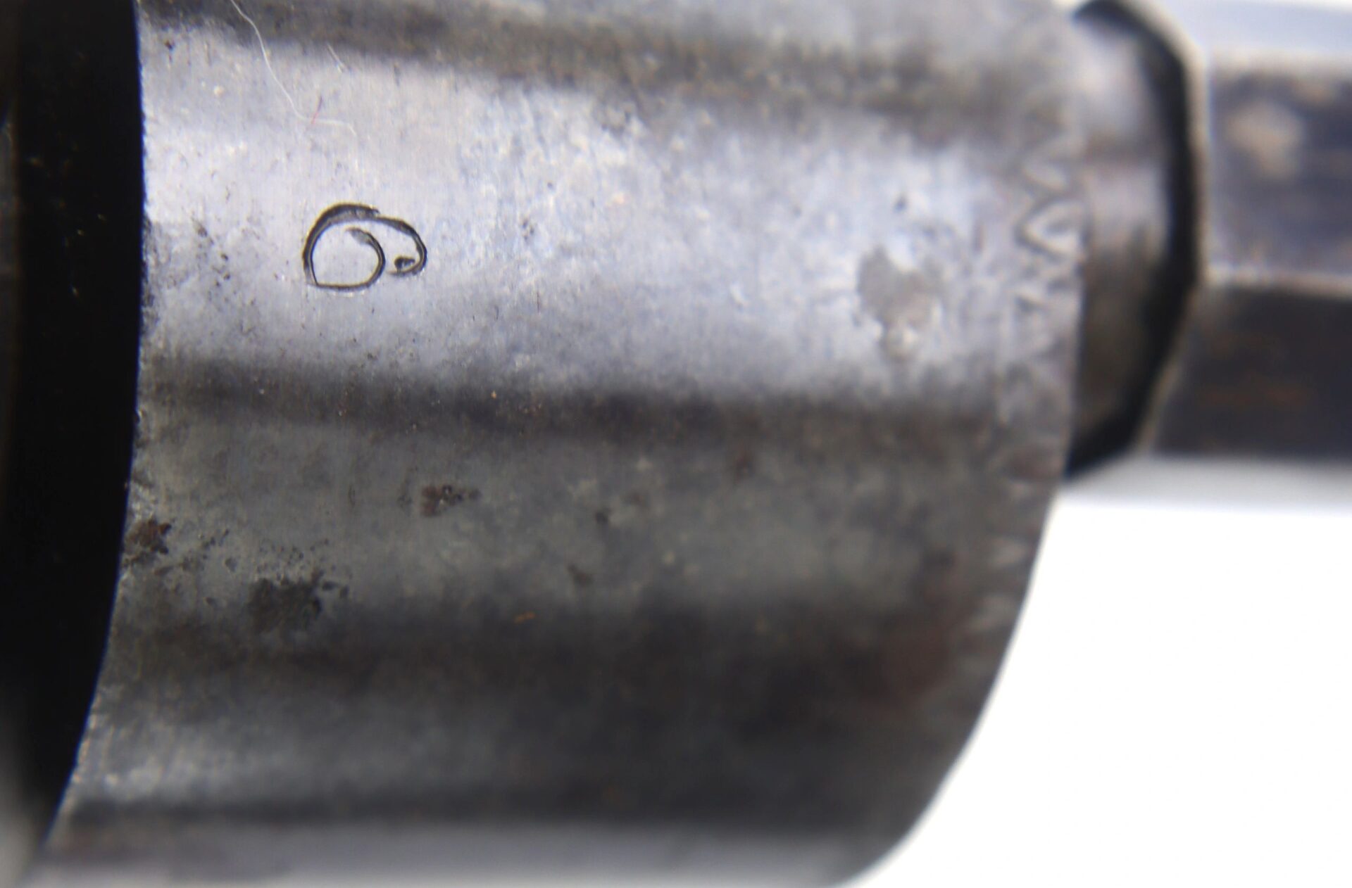 Close-up view of a metallic cylindrical surface on A Transitional Revolver by Clough & Son Bath, showing a small engraved number "6".