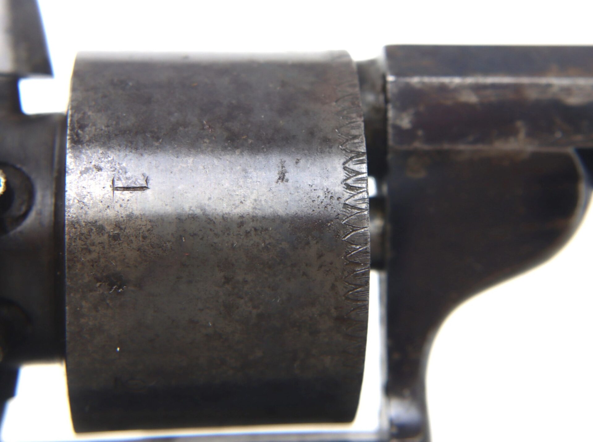 Close-up view of a dark metal cylinder with notched edge and wear marks from a Transitional Revolver by Clough & Son Bath.