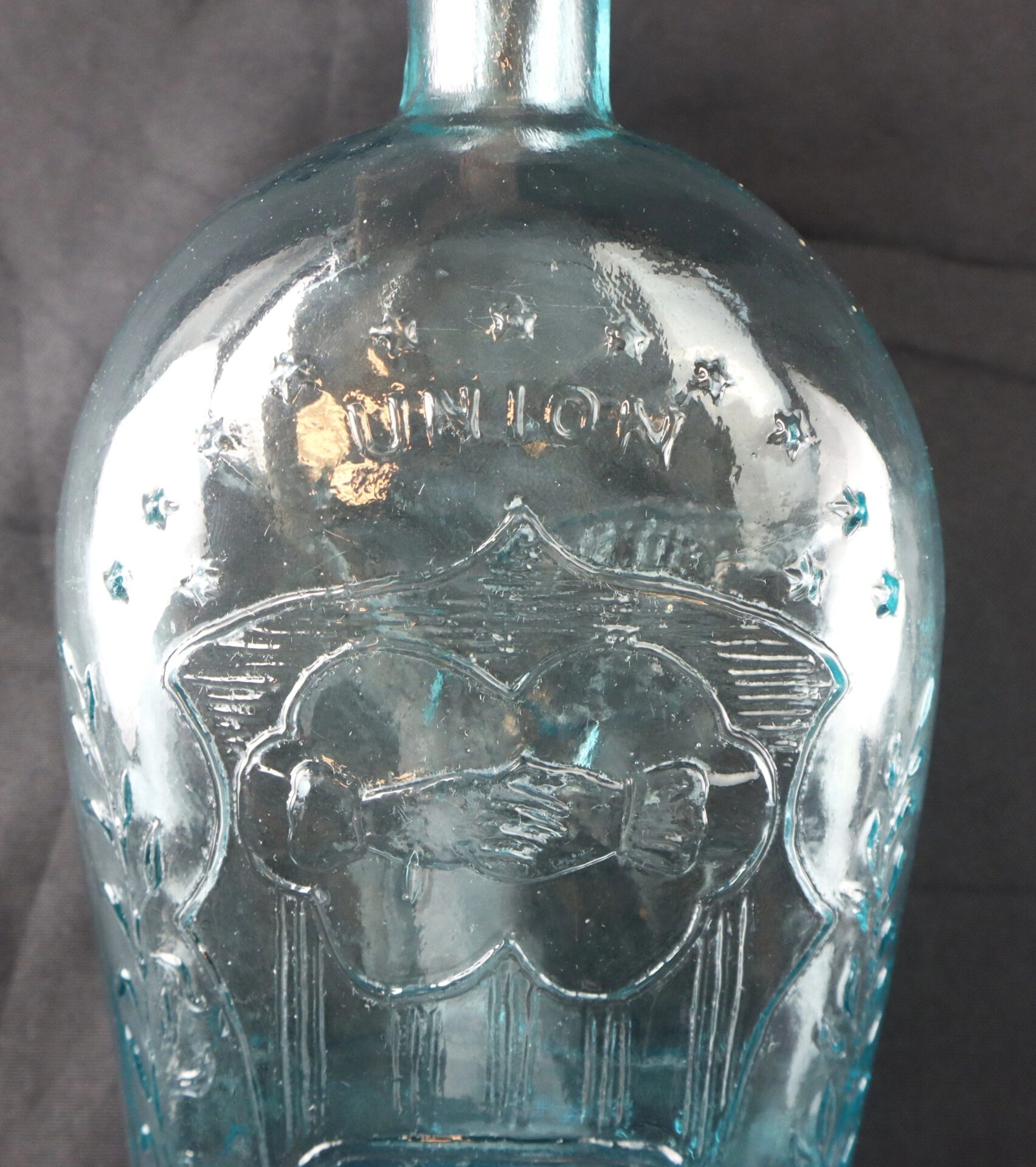 Civil War-Era Union Patriotic Flask in aqua blue glass, embossed with "UNION" above two clasped hands, radiating lines, and stars surrounding the design.