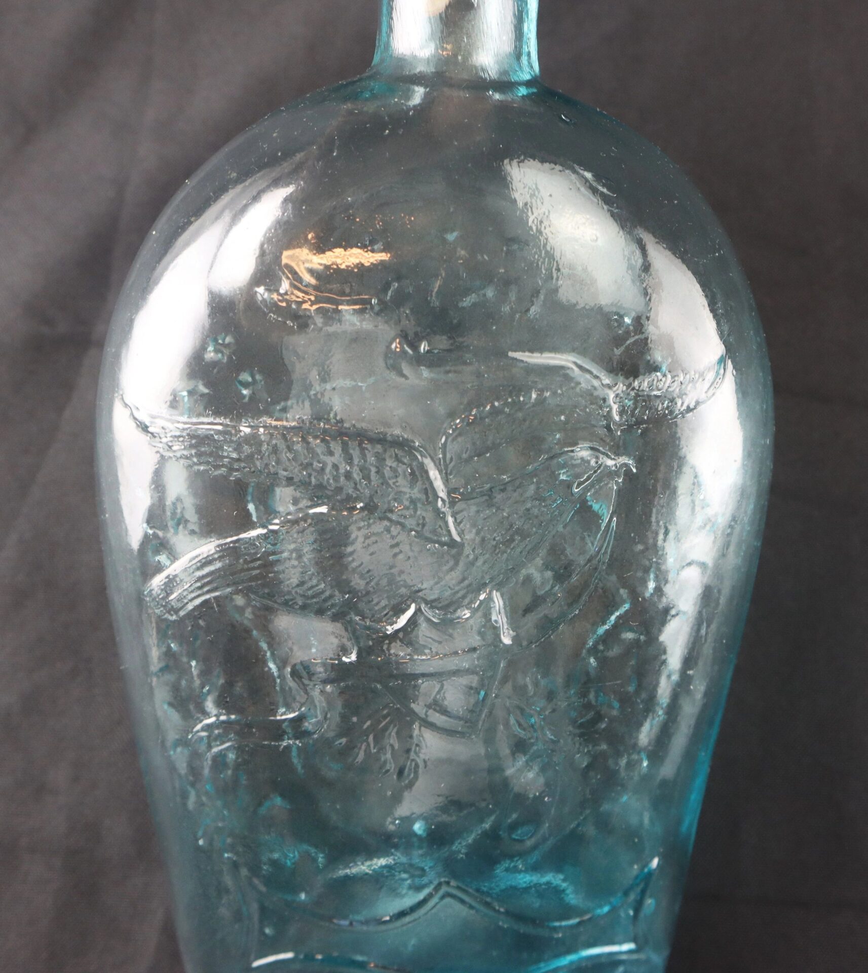 An aqua blue Civil War-era Union patriotic flask, embossed with an eagle in flight, is displayed against a dark background.
