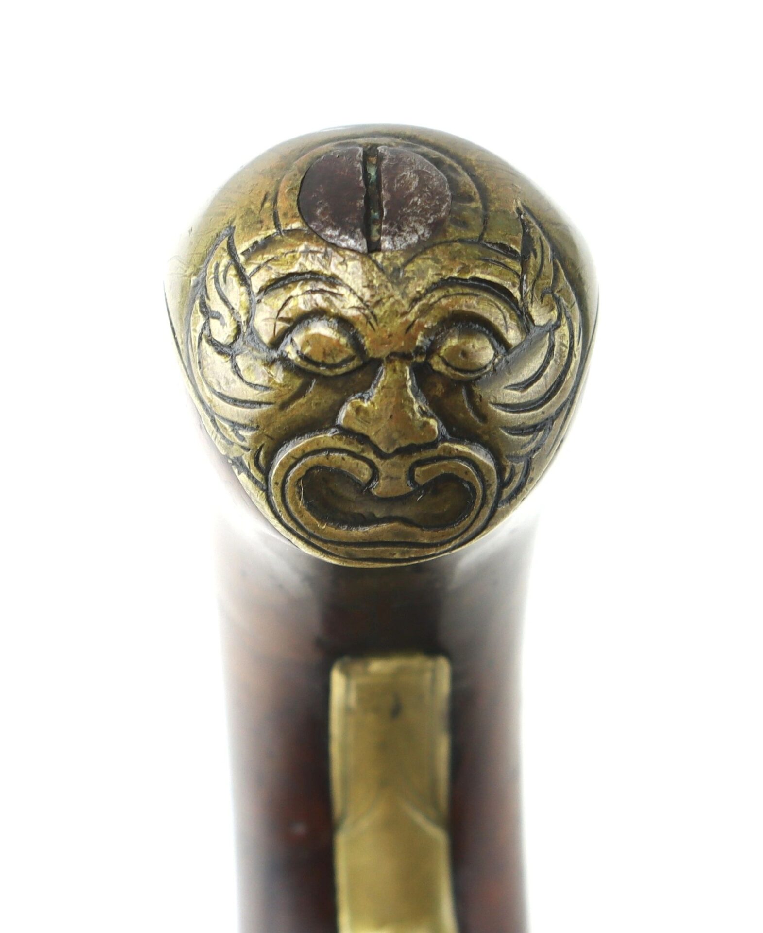 Close-up of the brass butt cap on an English Pistol with Brass Barrel, featuring a grotesque engraved mask at the end of its wooden handle.