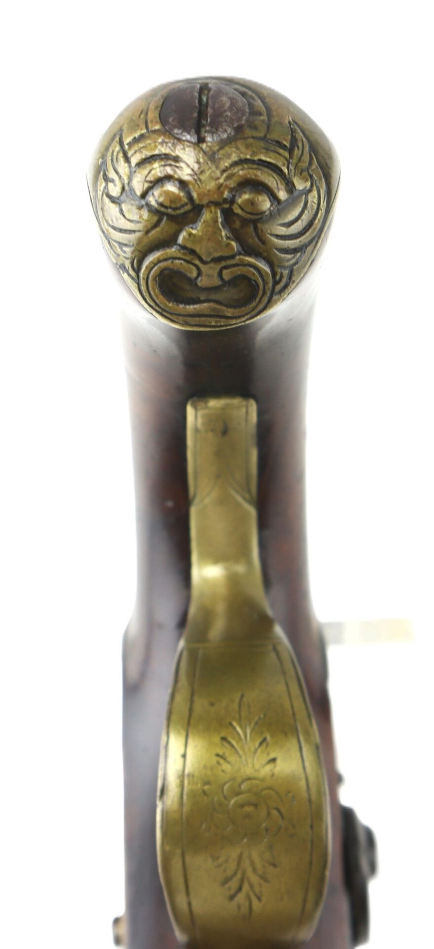 Close-up view of the English Pistol with Brass Barrel, featuring an ornate grip and a grotesque mask design engraved on the brass butt cap.