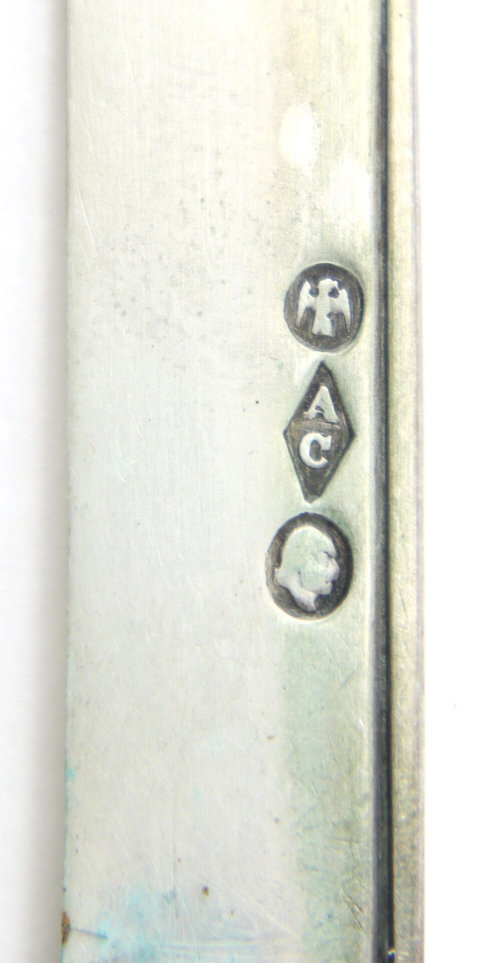 Close-up of three stamped hallmarks on the British Sterling Silver Folding Fruit Knife – Floral Repoussé Handle: a figure, "A C" in a diamond, and a head profile in a circle on the metal surface.