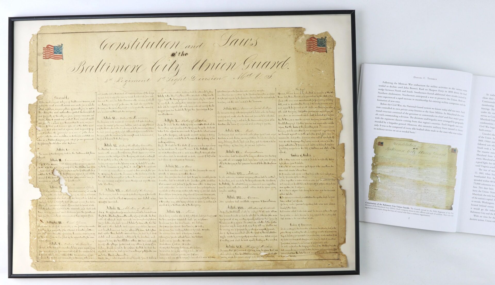 A framed "Constitution and Laws of the Baltimore City Union Guards (Baltimore, Maryland, c. 1860s)" is displayed alongside an open book showing a reproduction of this historical document.