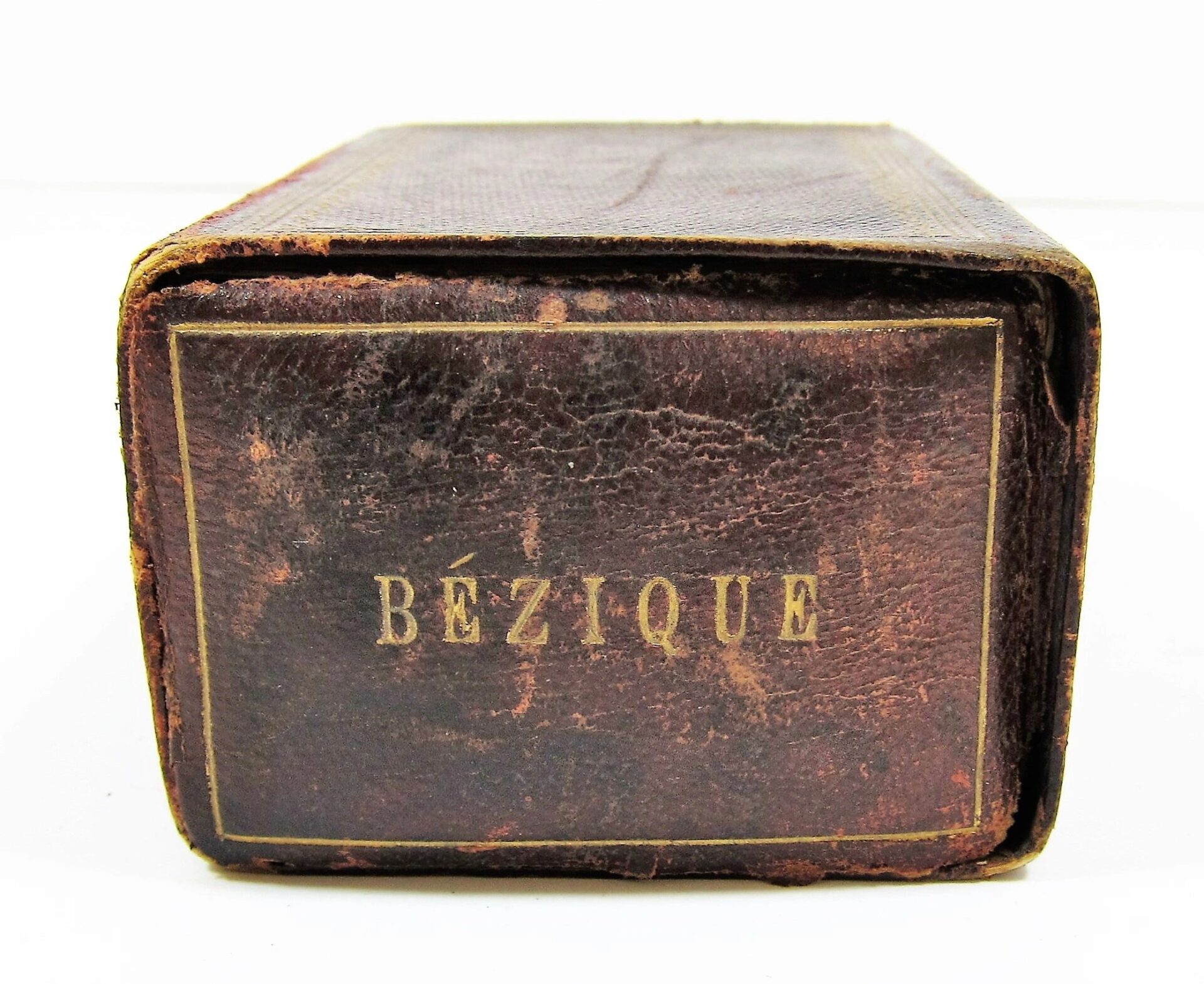 Close-up of a worn, brown leather box featuring the "Bezique Card Game" name stamped in gold letters on the front.