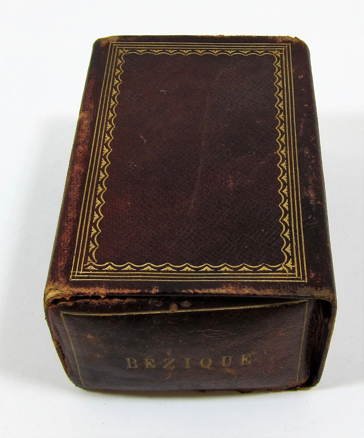 A worn brown leather box with gold trim, "Bezique Card Game" embossed on the spine.
