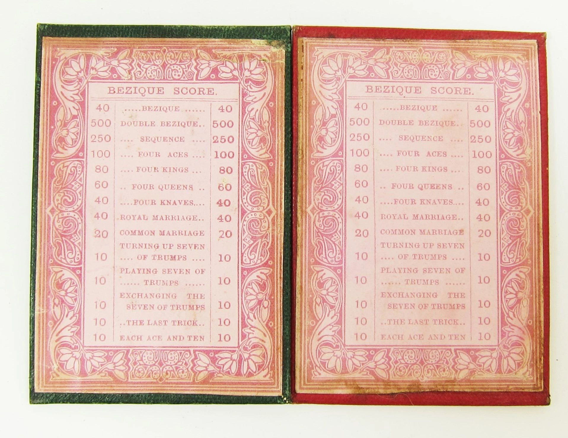 Open booklet for the Bezique Card Game featuring printed score tables with categories and point values in white text on a pink and red ornate background.