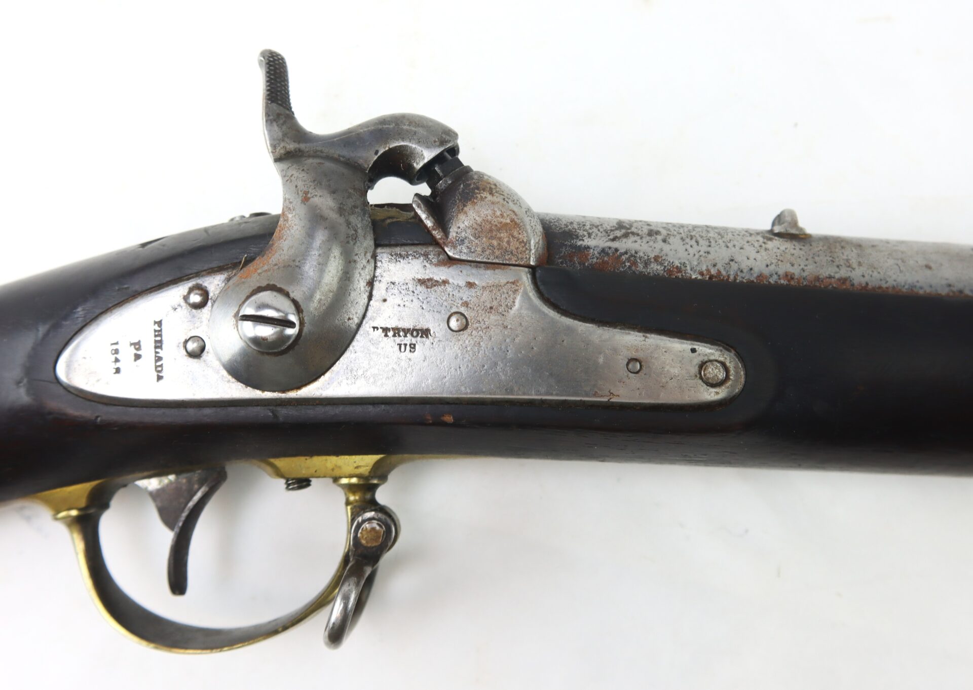 Close-up of an antique percussion cap musket, showing the lock mechanism, trigger, and manufacturer markings on a metal plate.