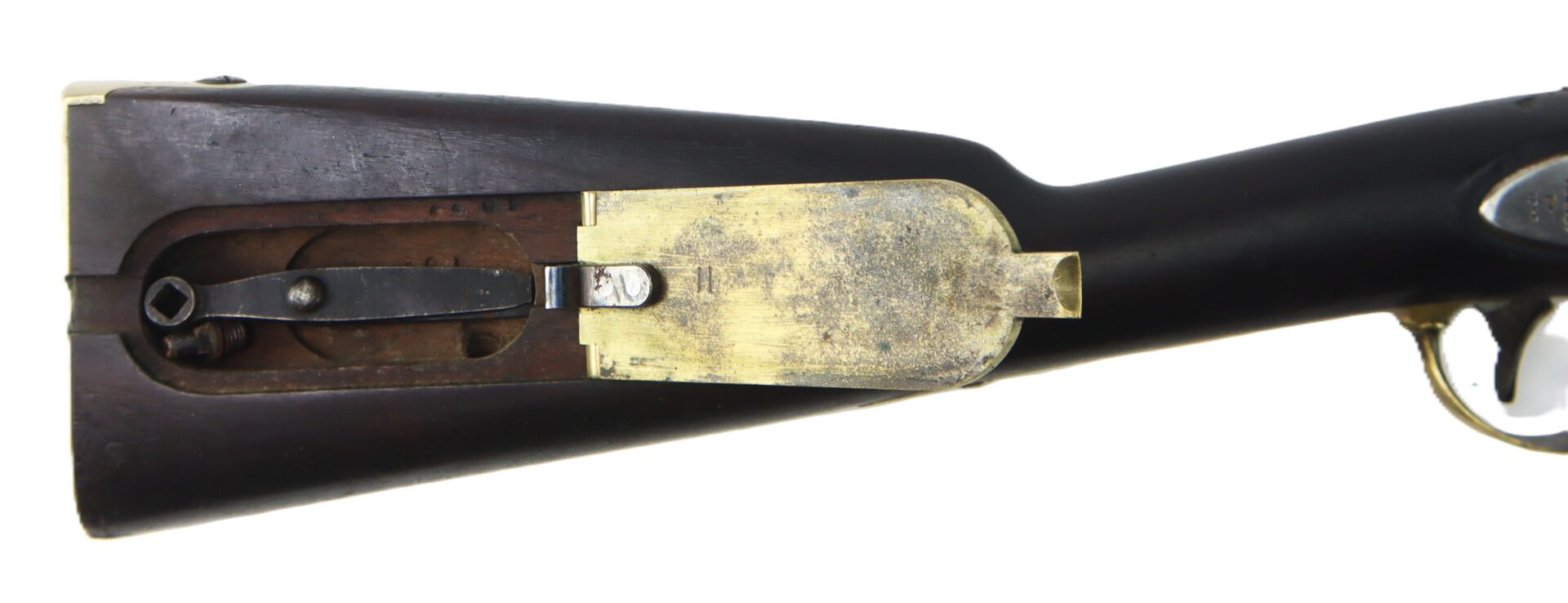 Close-up of a rifle buttstock with an open brass compartment cover, revealing an internal storage space.