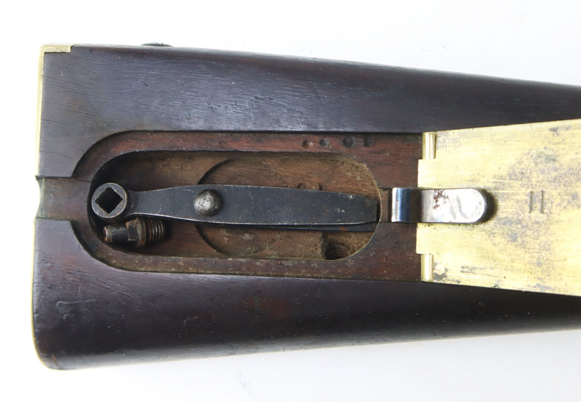 Close-up view of the underside of a rifle stock showing the brass patch box lid open, exposing internal metal components and mechanisms.